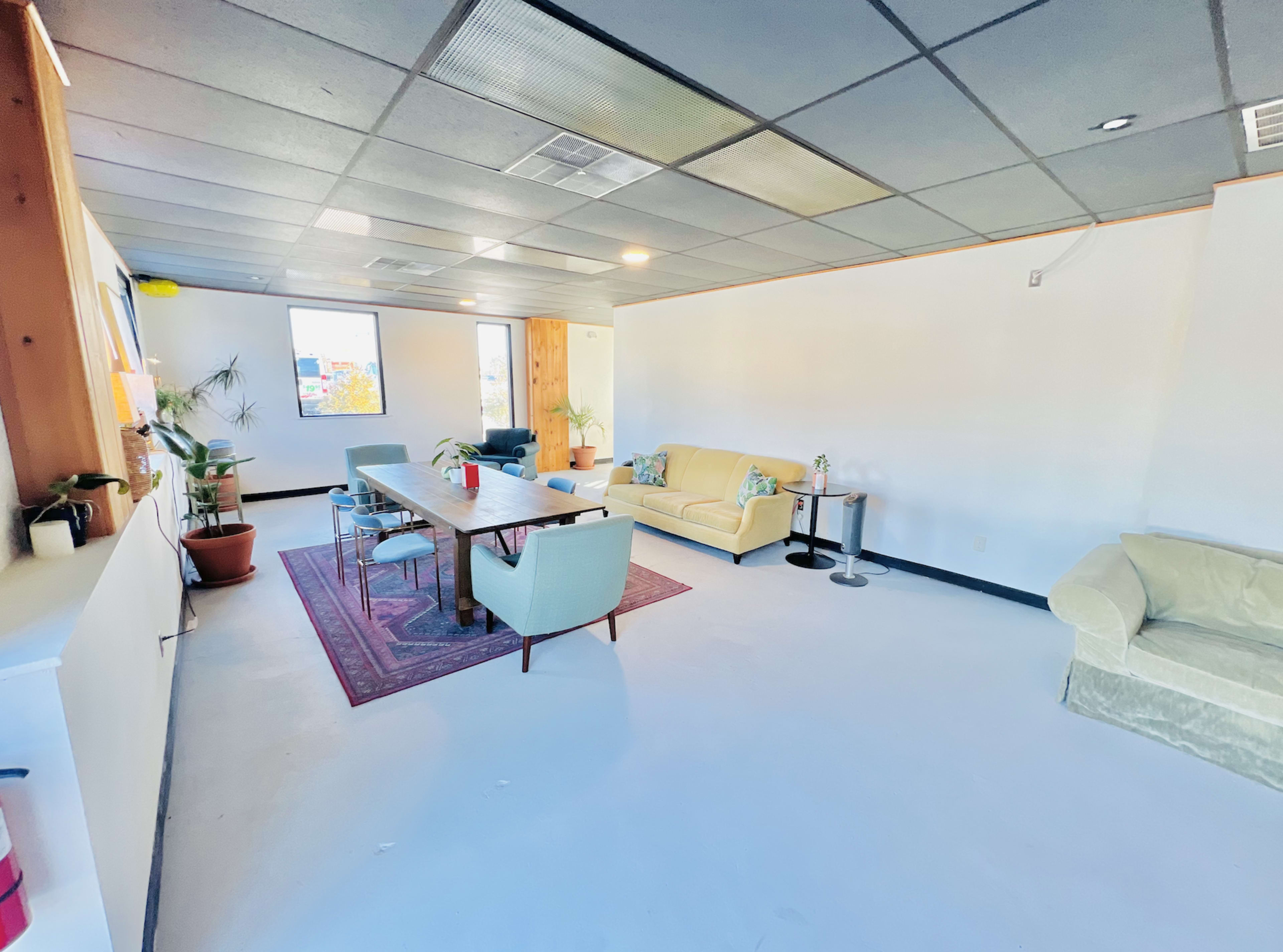 A spacious, modern lounge area with a large table, various seating options, and windows allowing natural light.