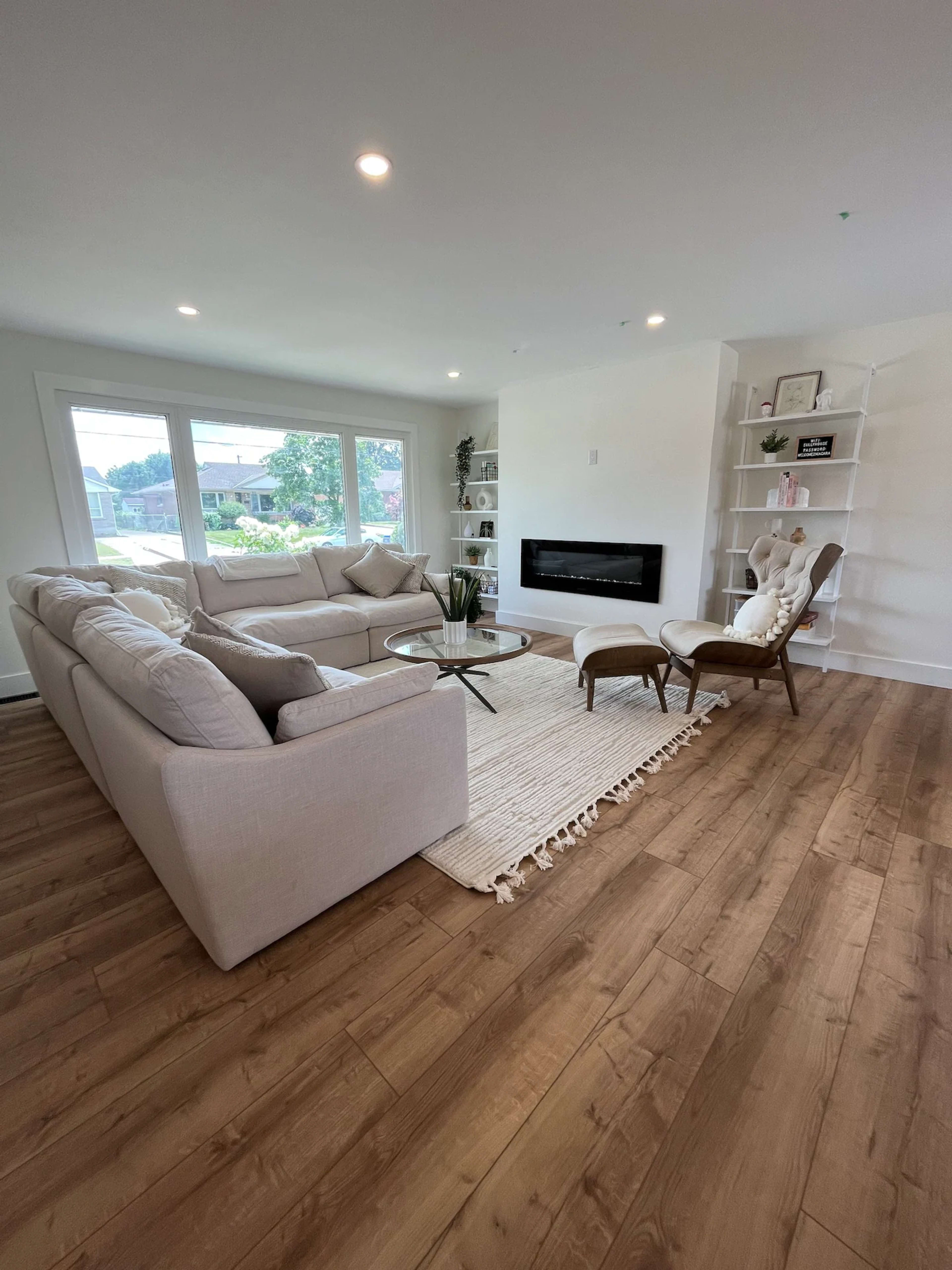 The living room features a light-colored sectional sofa, a glass coffee table, and a modern fireplace, all situated on a wooden floor with a woven rug.