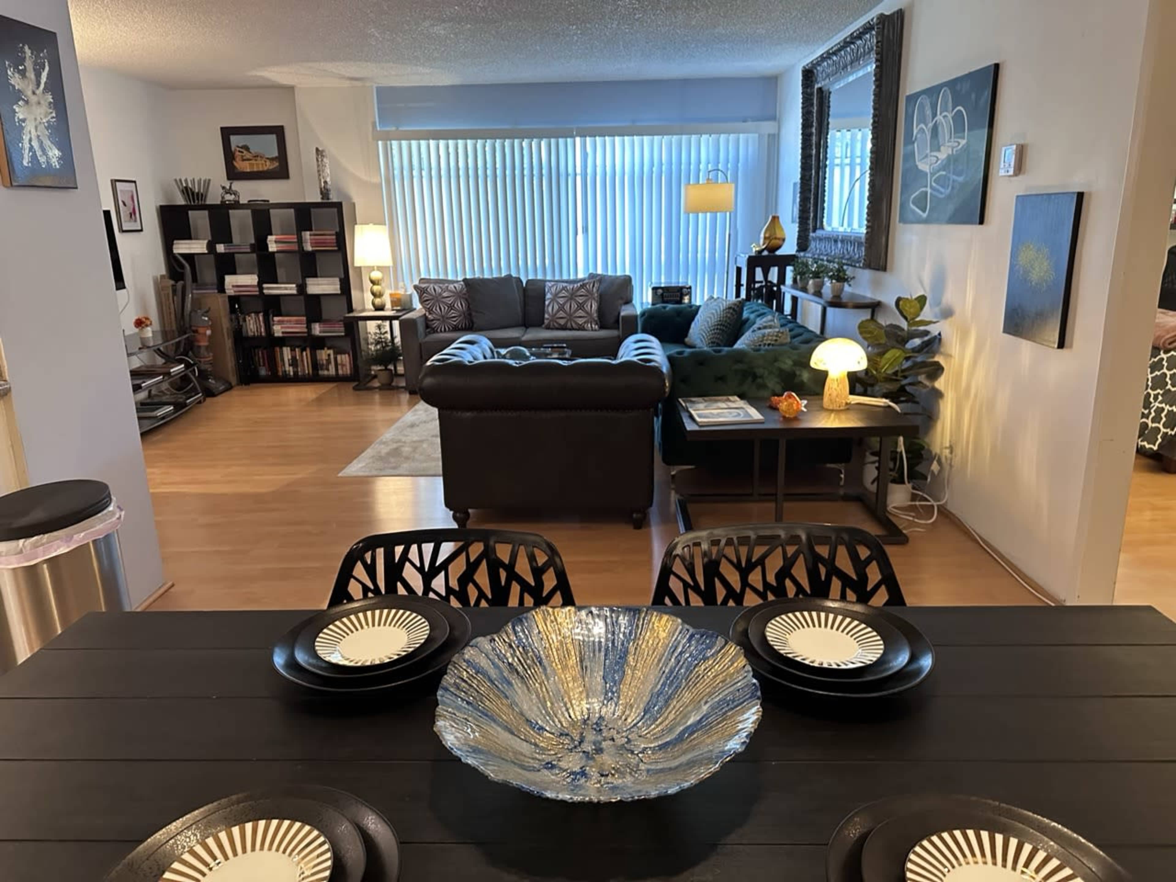 A modern living room and dining area are visible, featuring a dark wooden dining table with a glass bowl centerpiece, and a cozy seating arrangement with a large sectional couch.