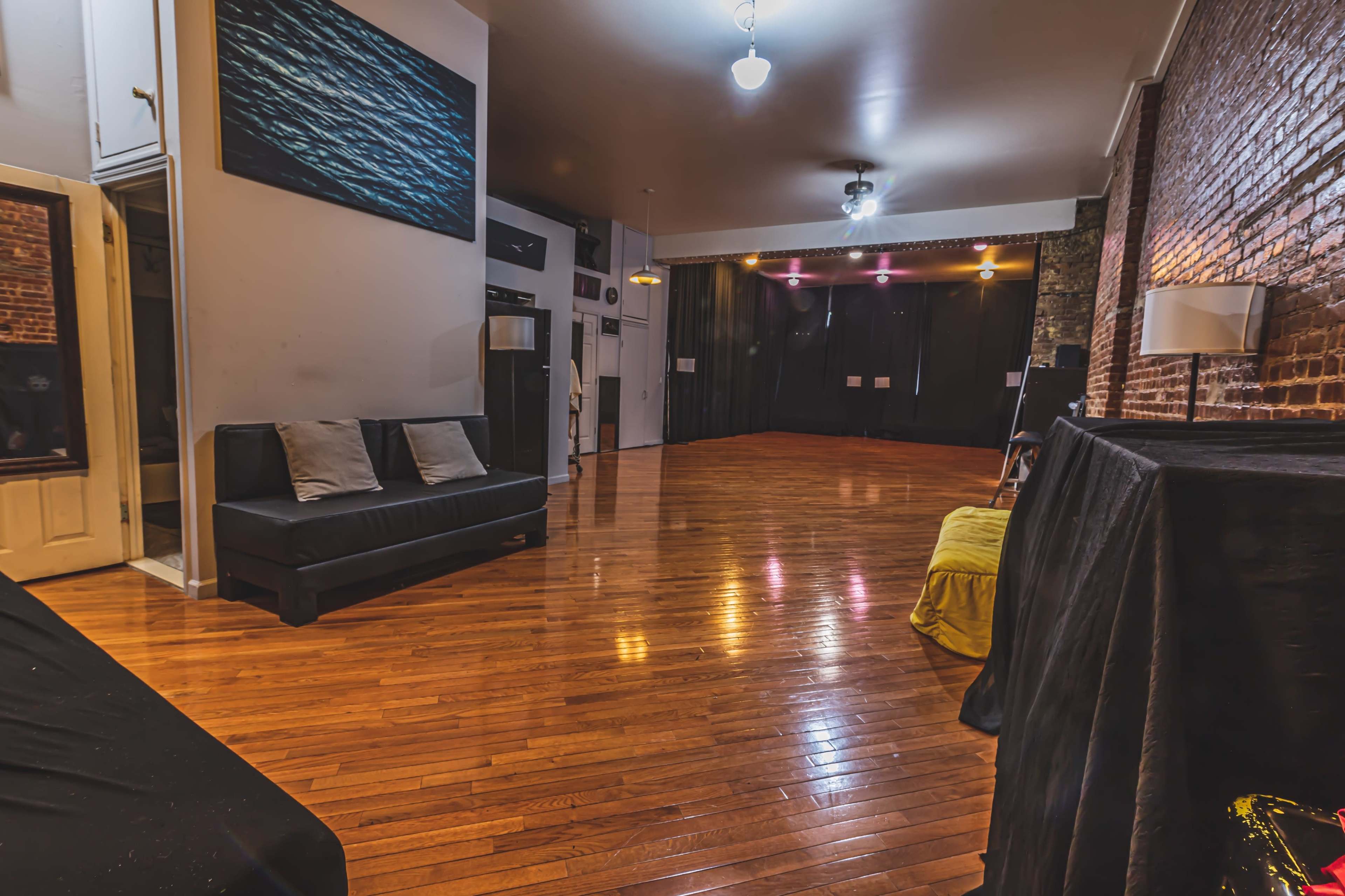 A spacious room with wooden floors, exposed brick walls, and a stage area illuminated by soft lights.
