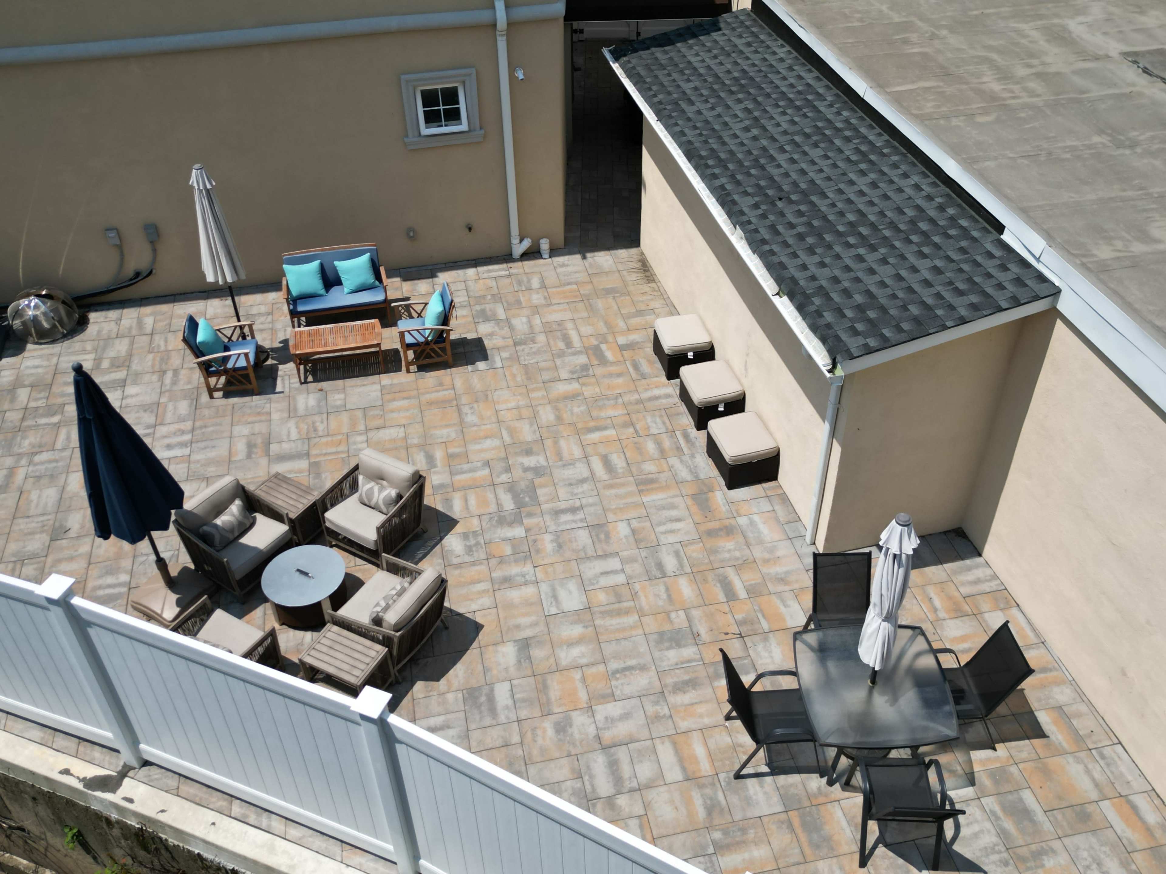 The image shows a patio area featuring several seating arrangements, including lounge chairs, a table with chairs, and a shaded umbrella.