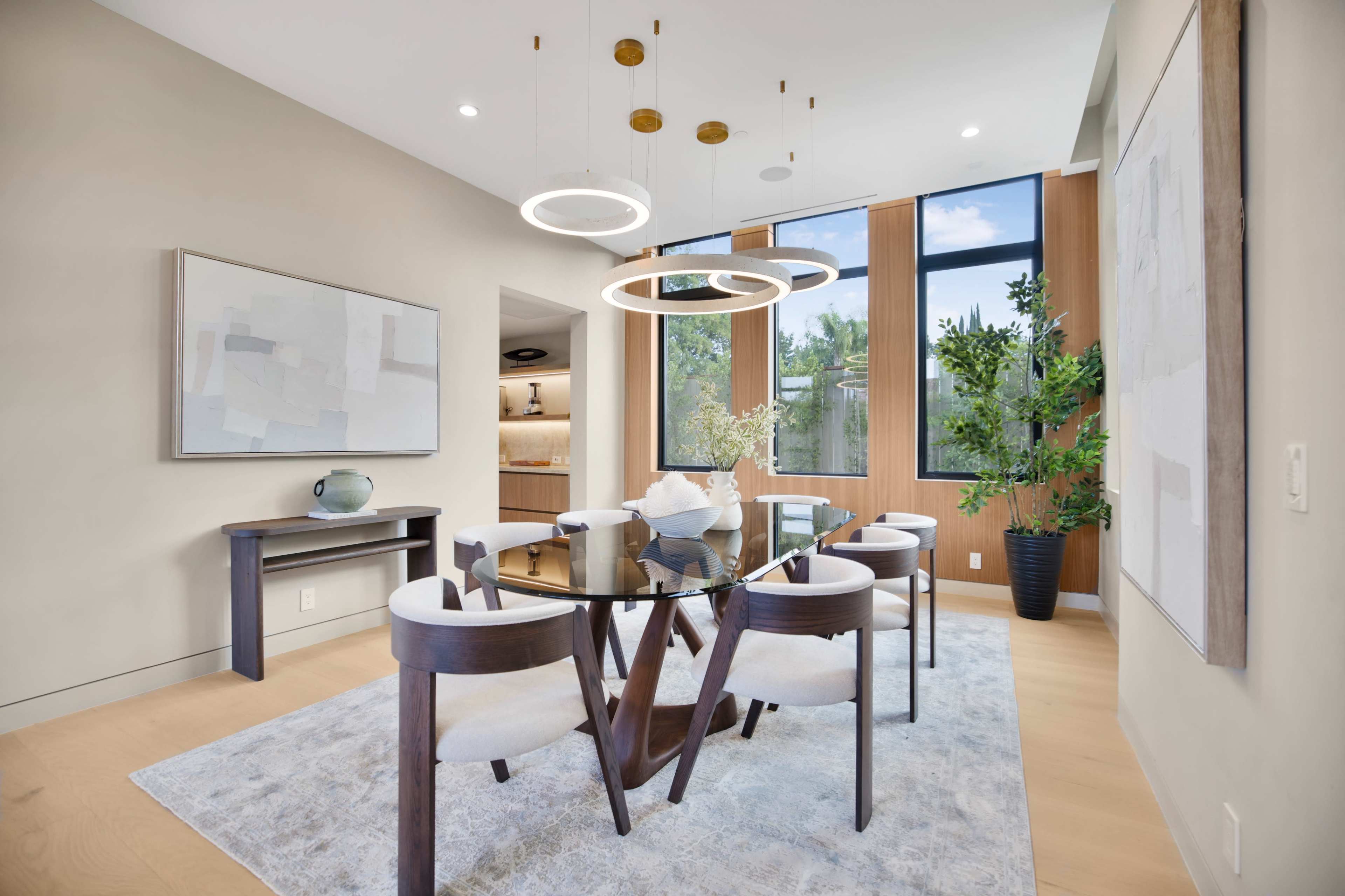 The image shows a modern dining room featuring a circular table surrounded by four chairs, with a large window allowing natural light to illuminate the space.