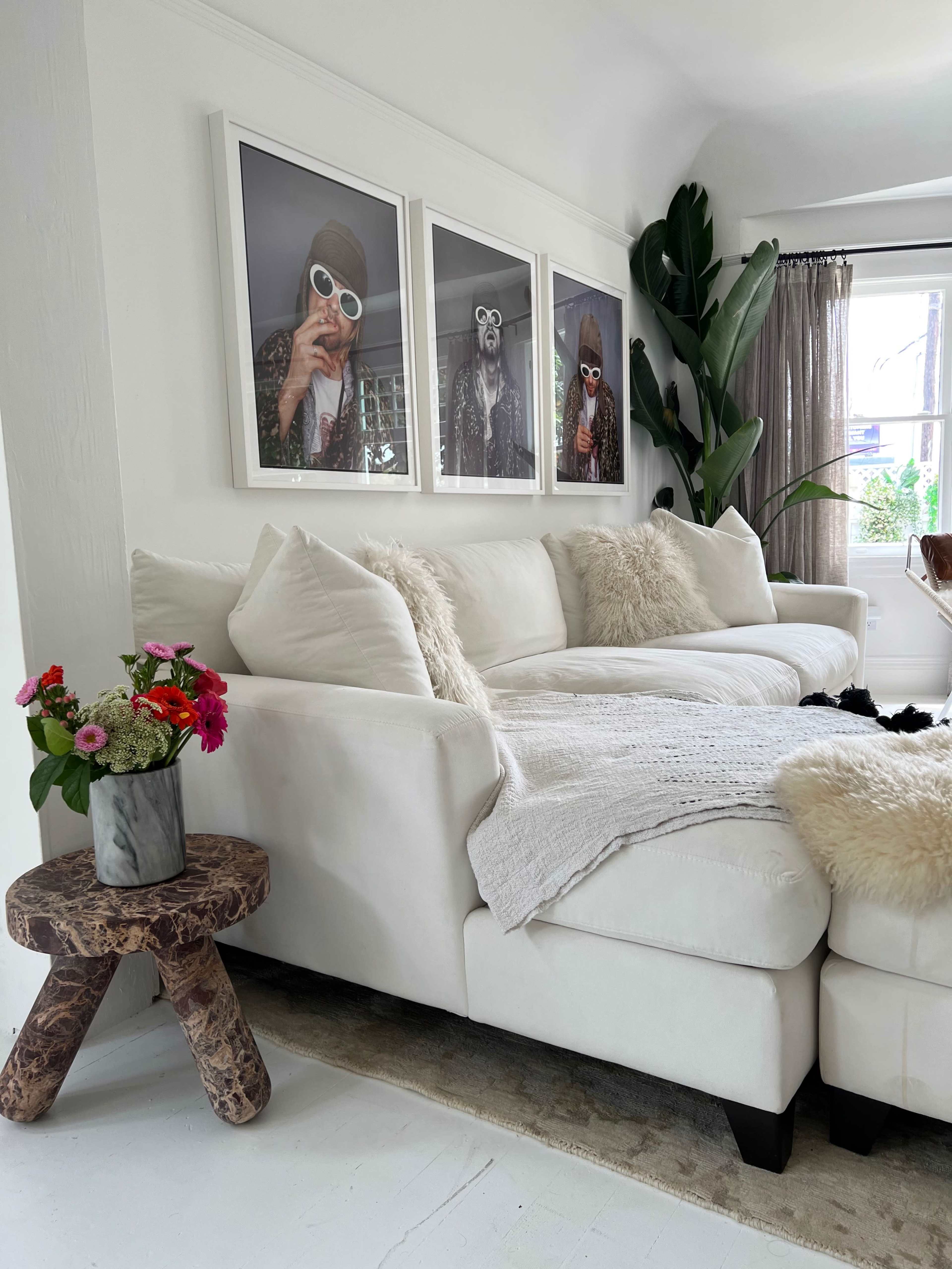 A white sectional sofa is positioned in a bright room, adorned with framed photographs on the wall and a small table holding a vase of colorful flowers.