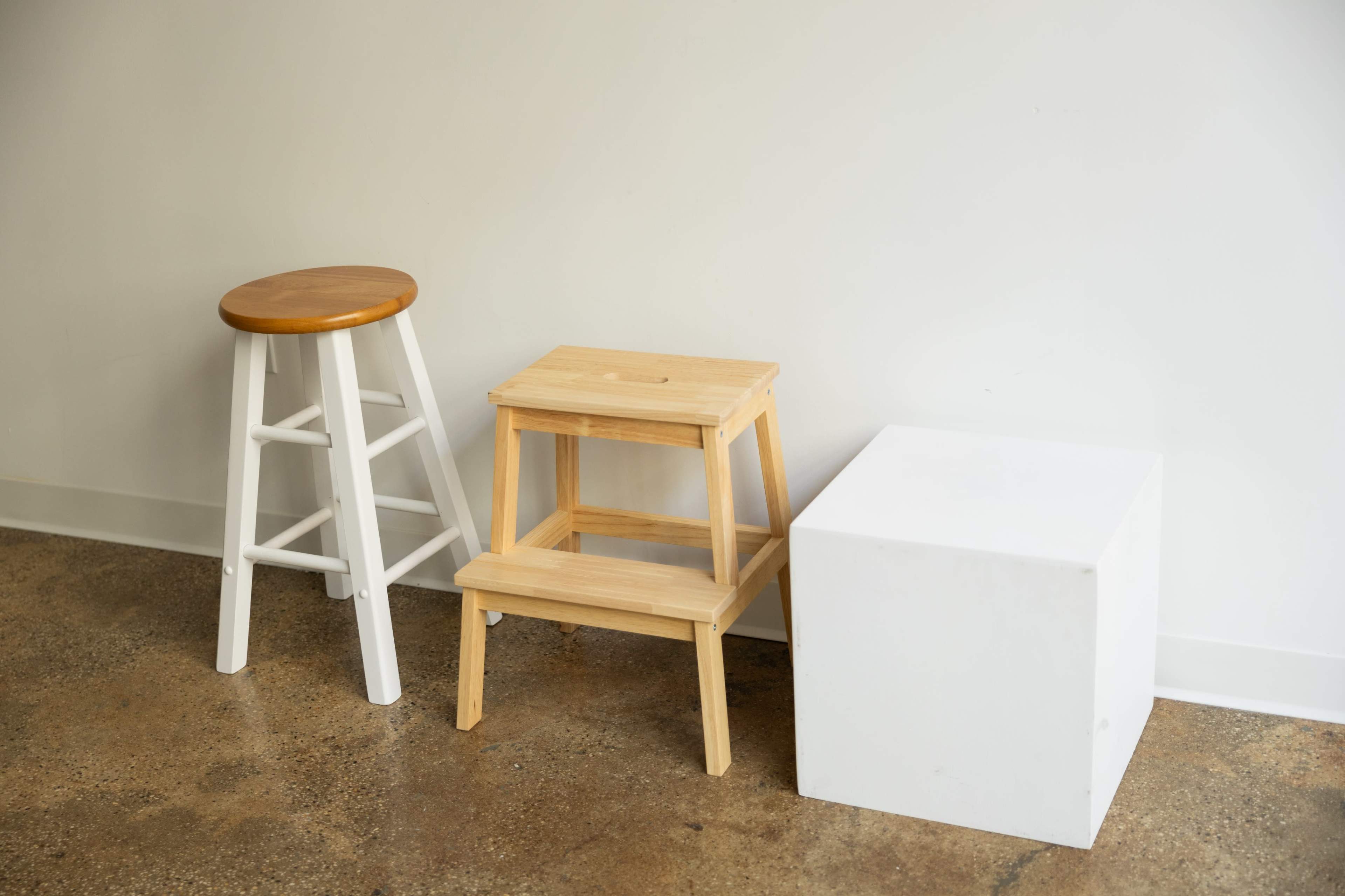 The image shows three types of seating and storage: a white wooden stool with a round wooden top, a wooden step stool, and a plain white cube.