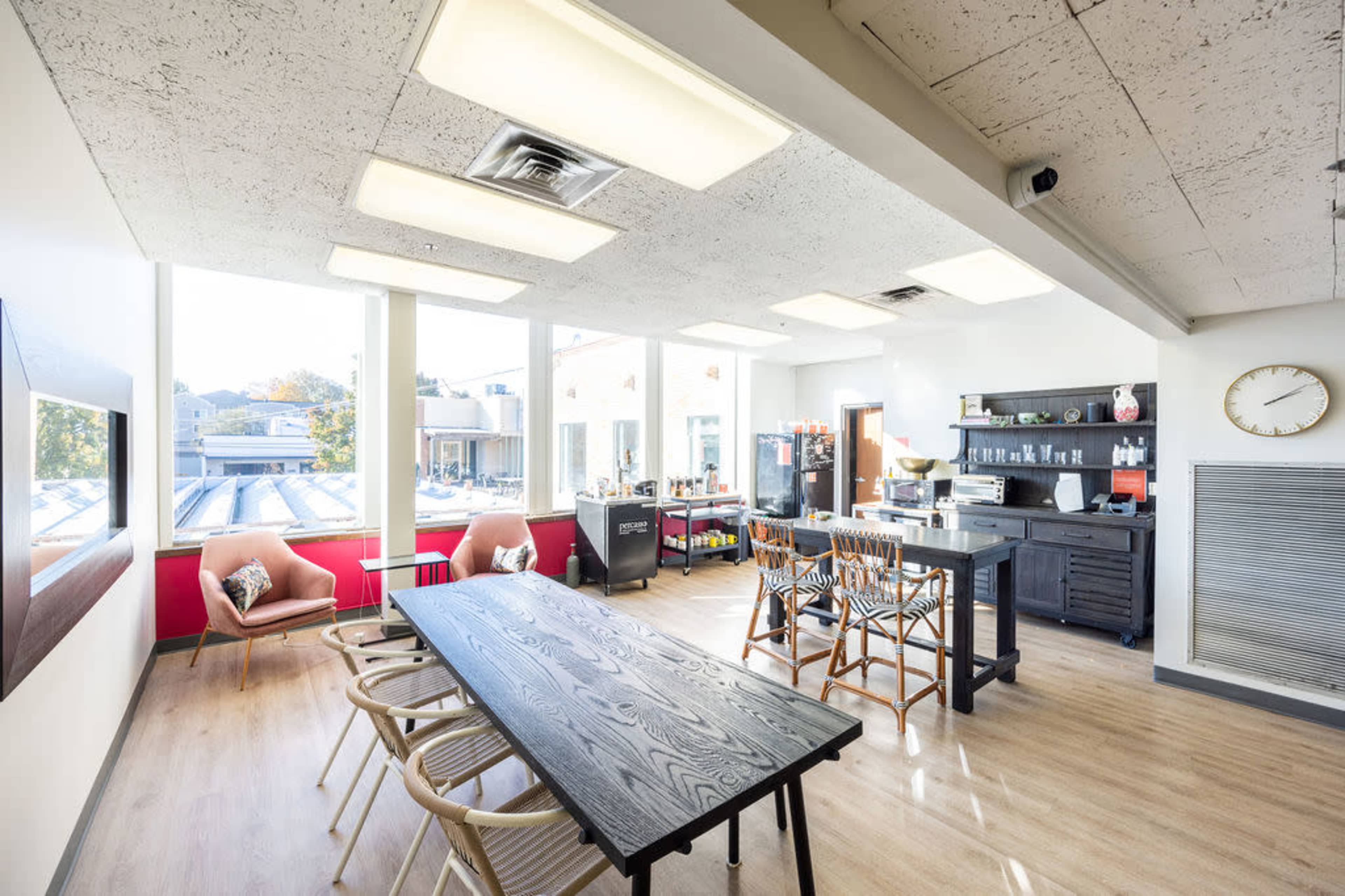 A bright, modern kitchen and dining area features a large table surrounded by chairs, with windows showcasing an outdoor view.