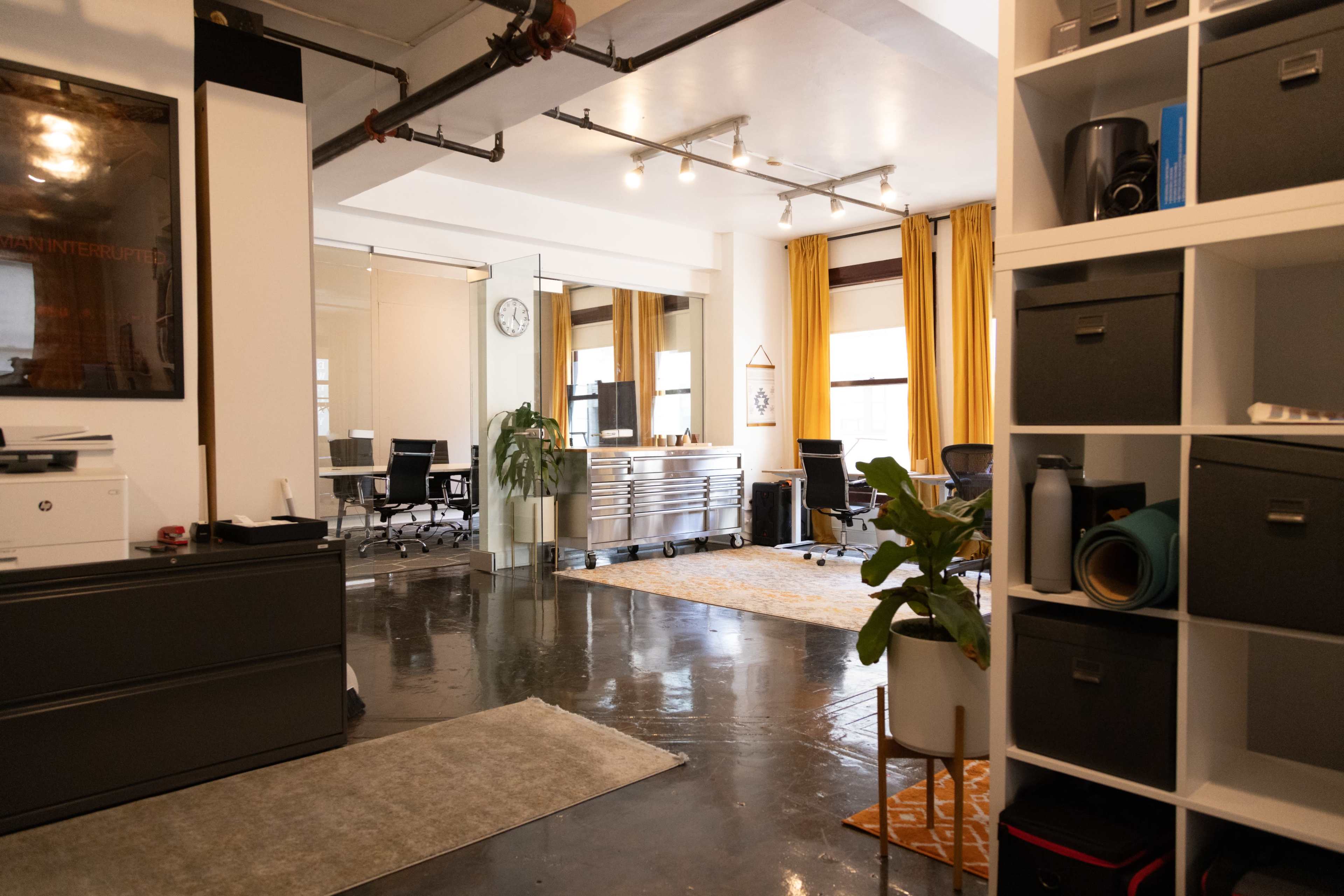 The image shows an office space with polished concrete floors, a mirrored wall, and furniture including filing cabinets, plants, and a clock on the wall.