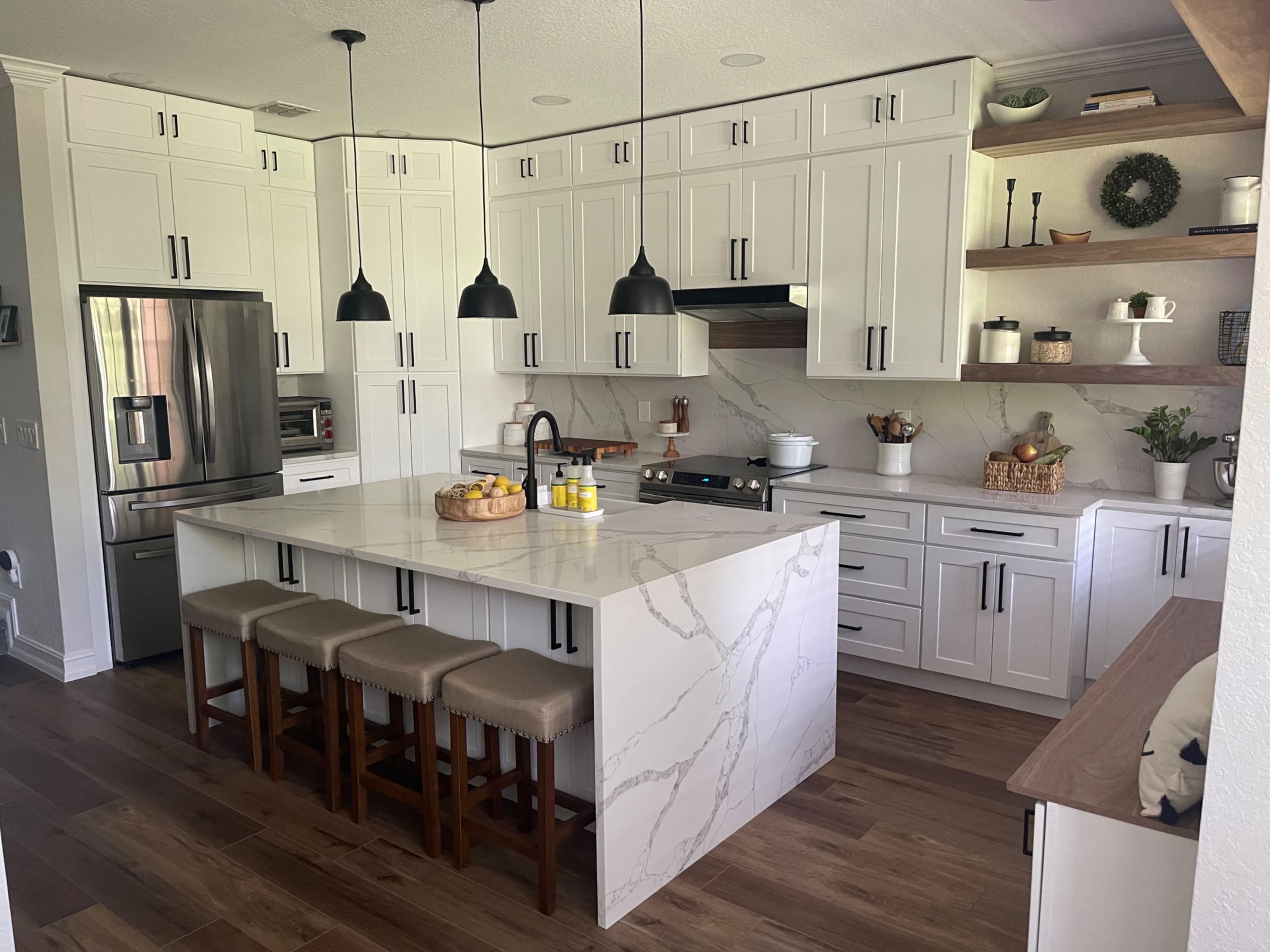 A modern kitchen features white cabinetry, a large marble island with seating, and stainless steel appliances.