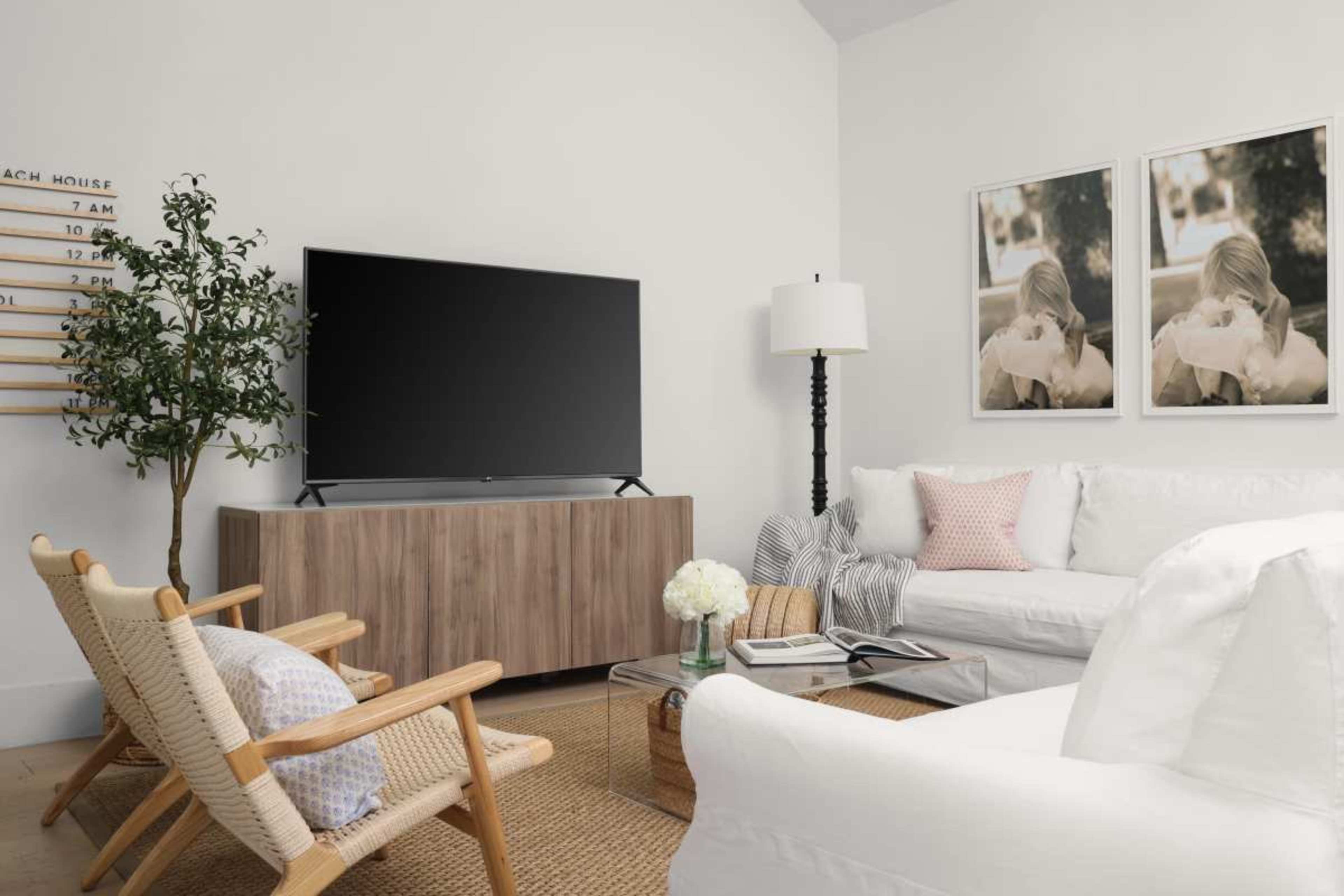 A modern living room features a large television on a wooden console, two armchairs, and framed photographs on the wall.