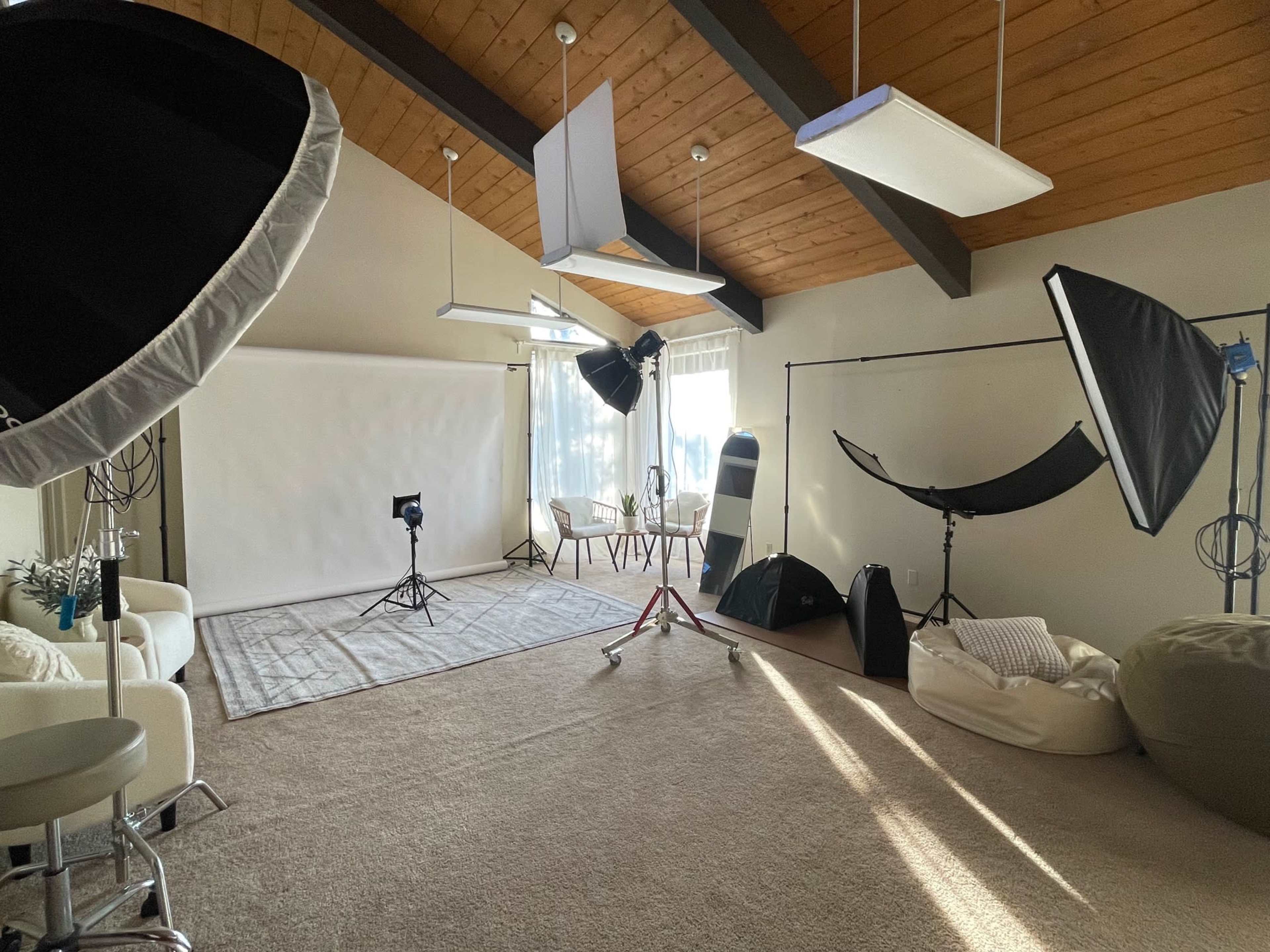 The image shows a photography studio with various lighting equipment, a backdrop, and seating arranged under a wooden ceiling.