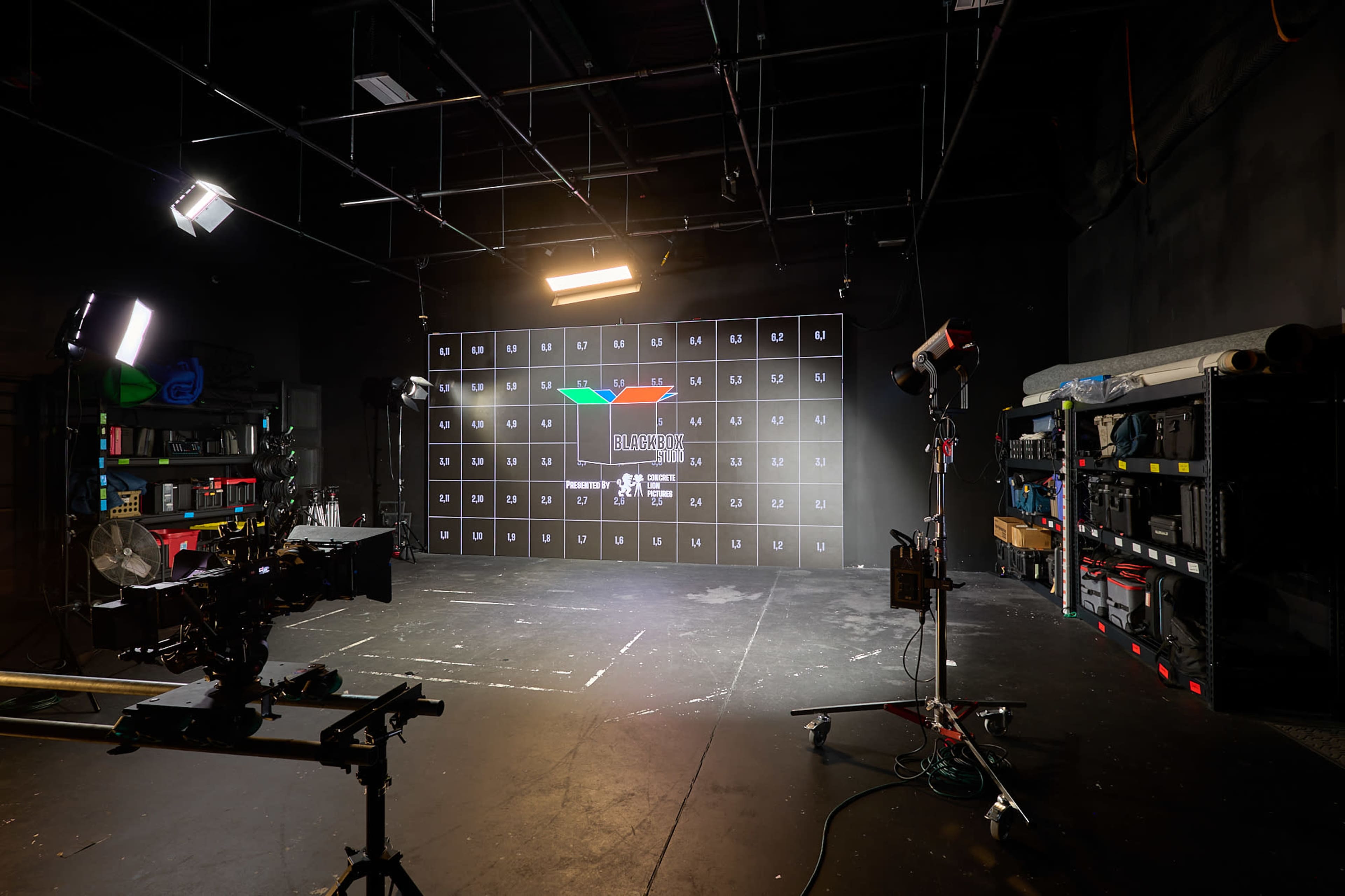 The image shows a dark studio space equipped with a grid wall display and various lighting and filming equipment positioned around the area.