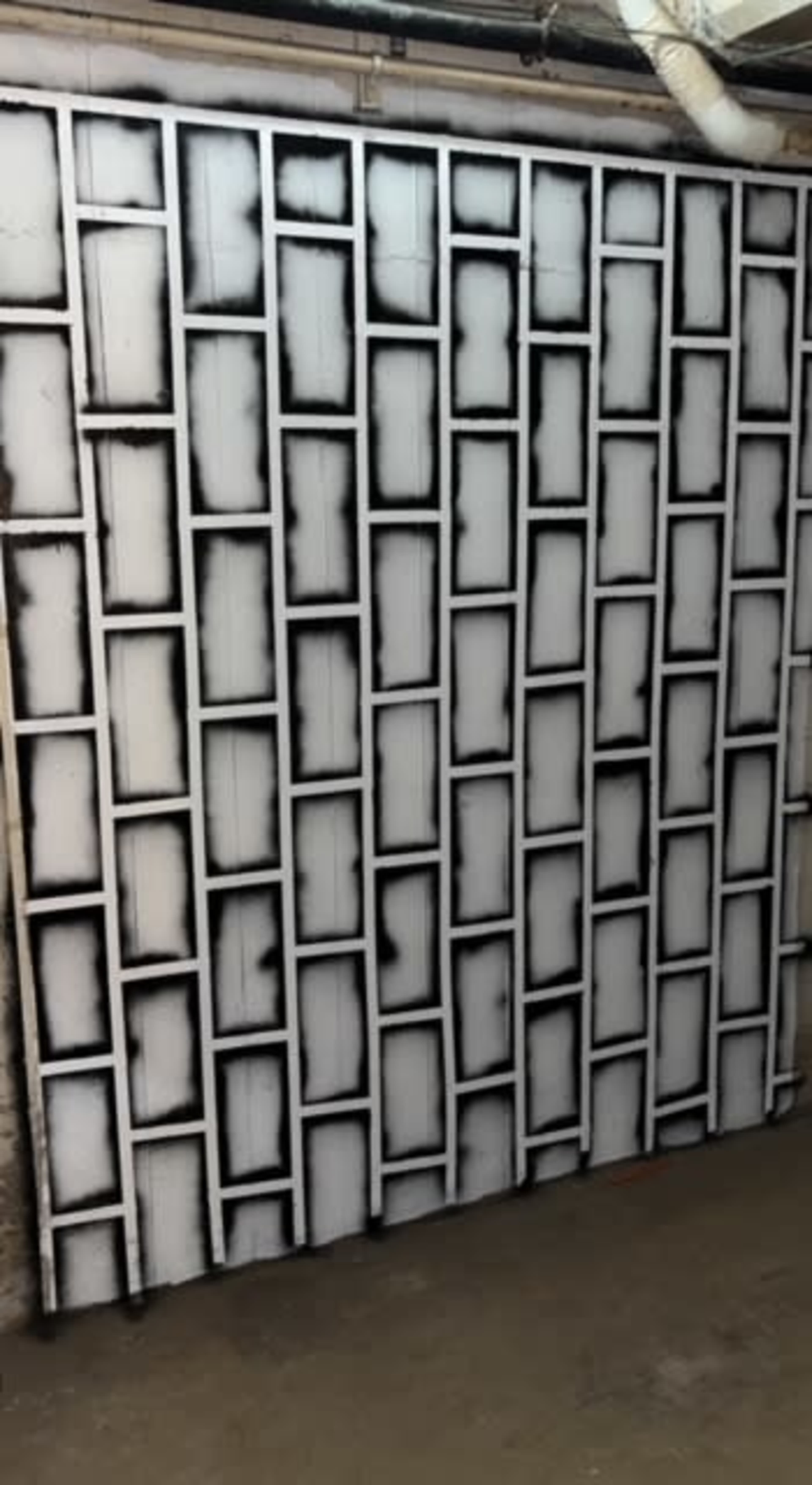A wall in a basement with a spray-painted design of rectangular frames outlined in black against a white background.