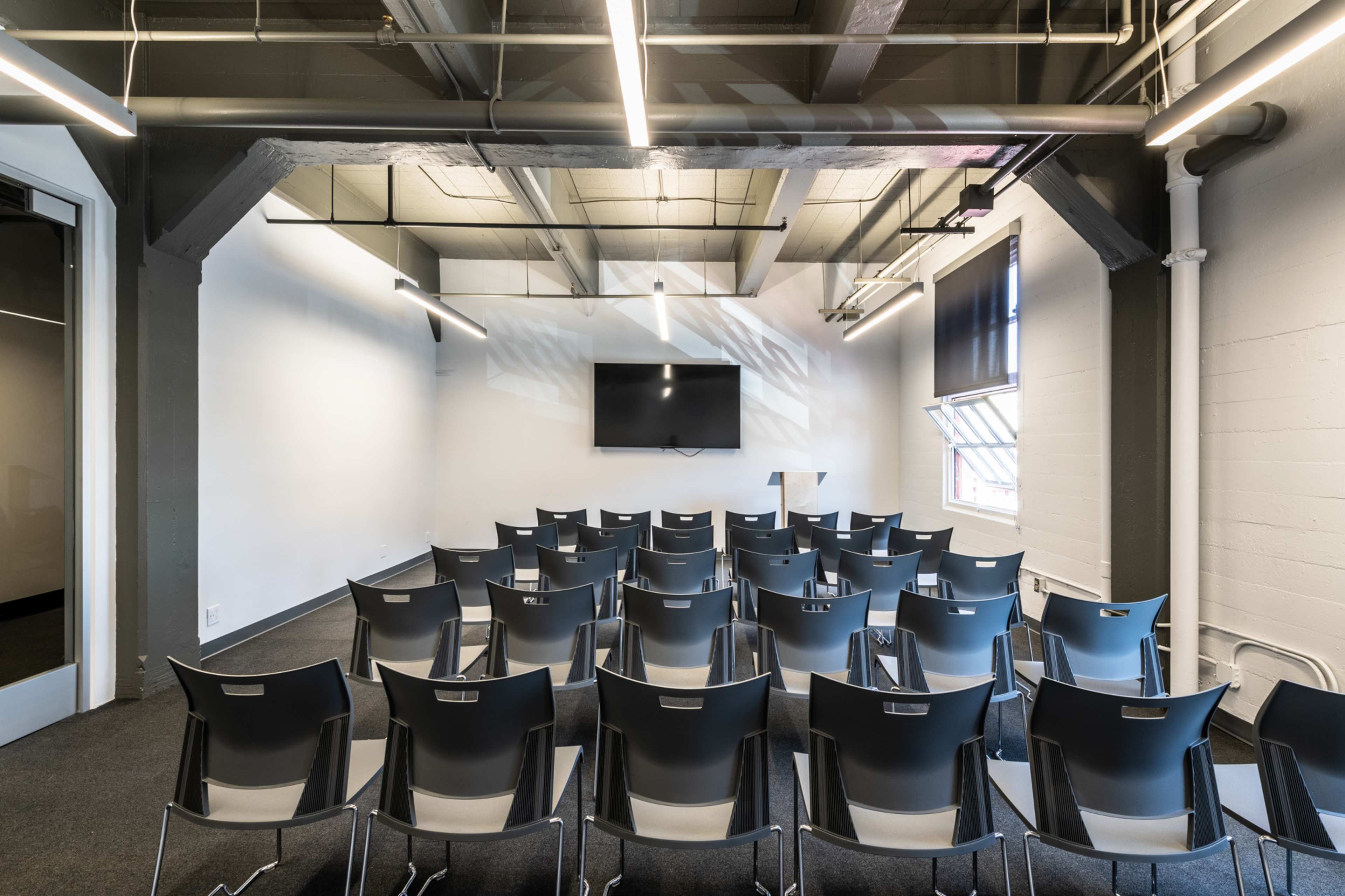 A meeting room features rows of metal chairs facing a wall-mounted television.