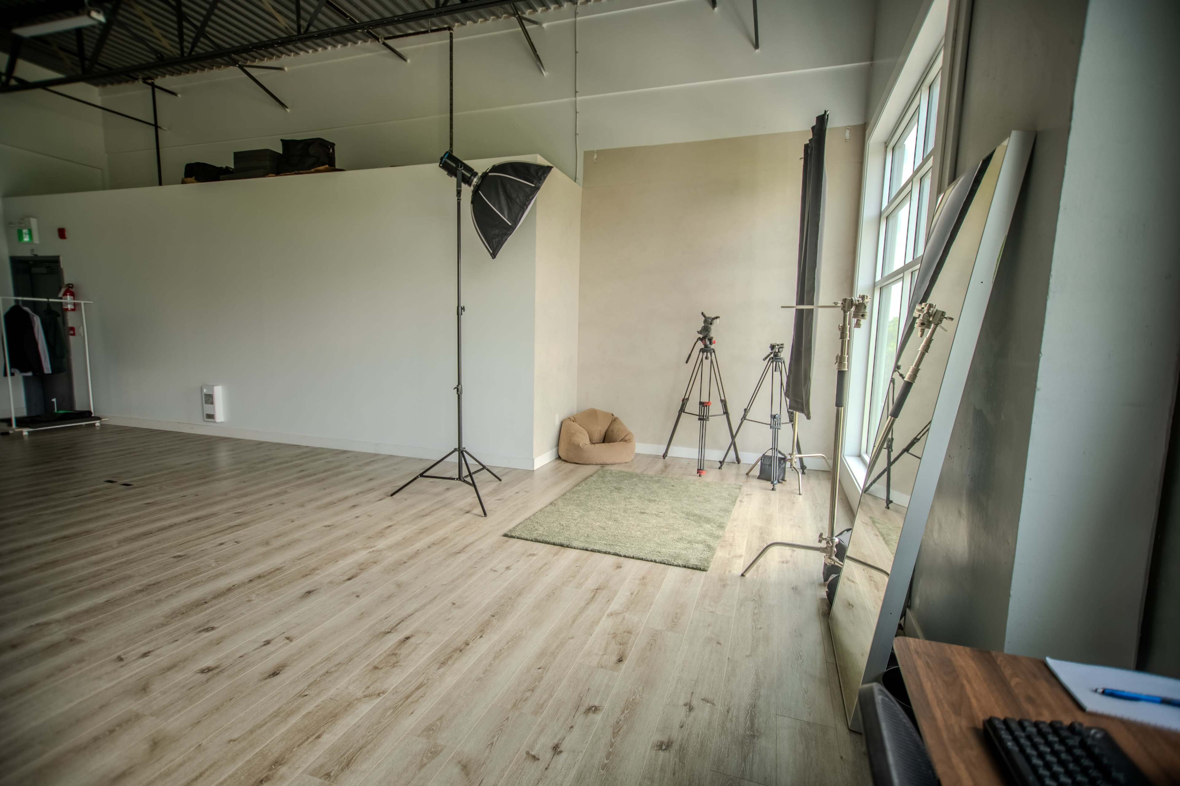 The image shows a spacious photography studio featuring tripods, lighting equipment, a soft seating area, and a large mirror against the wall.