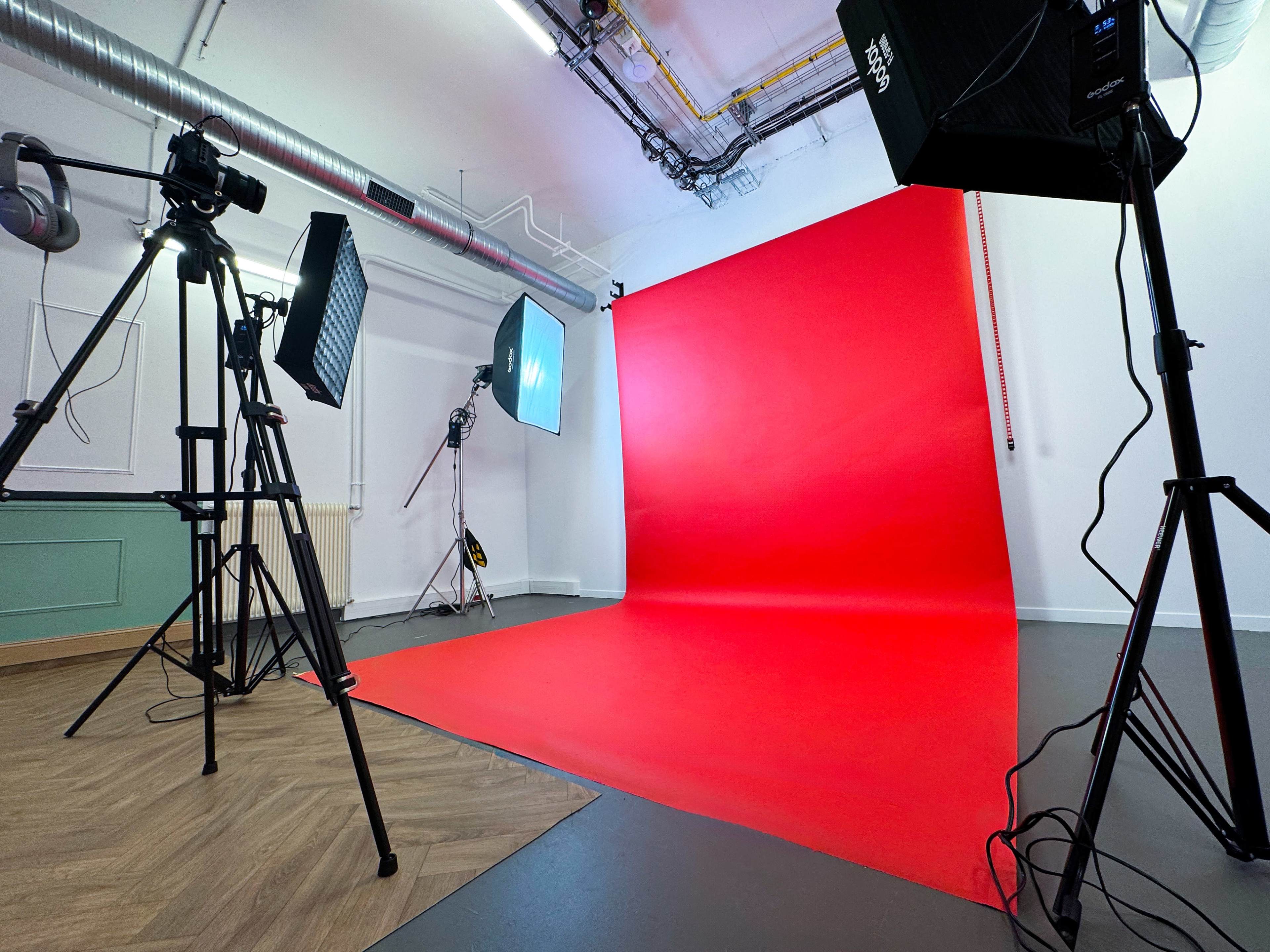 A photo studio is set up with a red backdrop and professional lighting equipment on tripods.