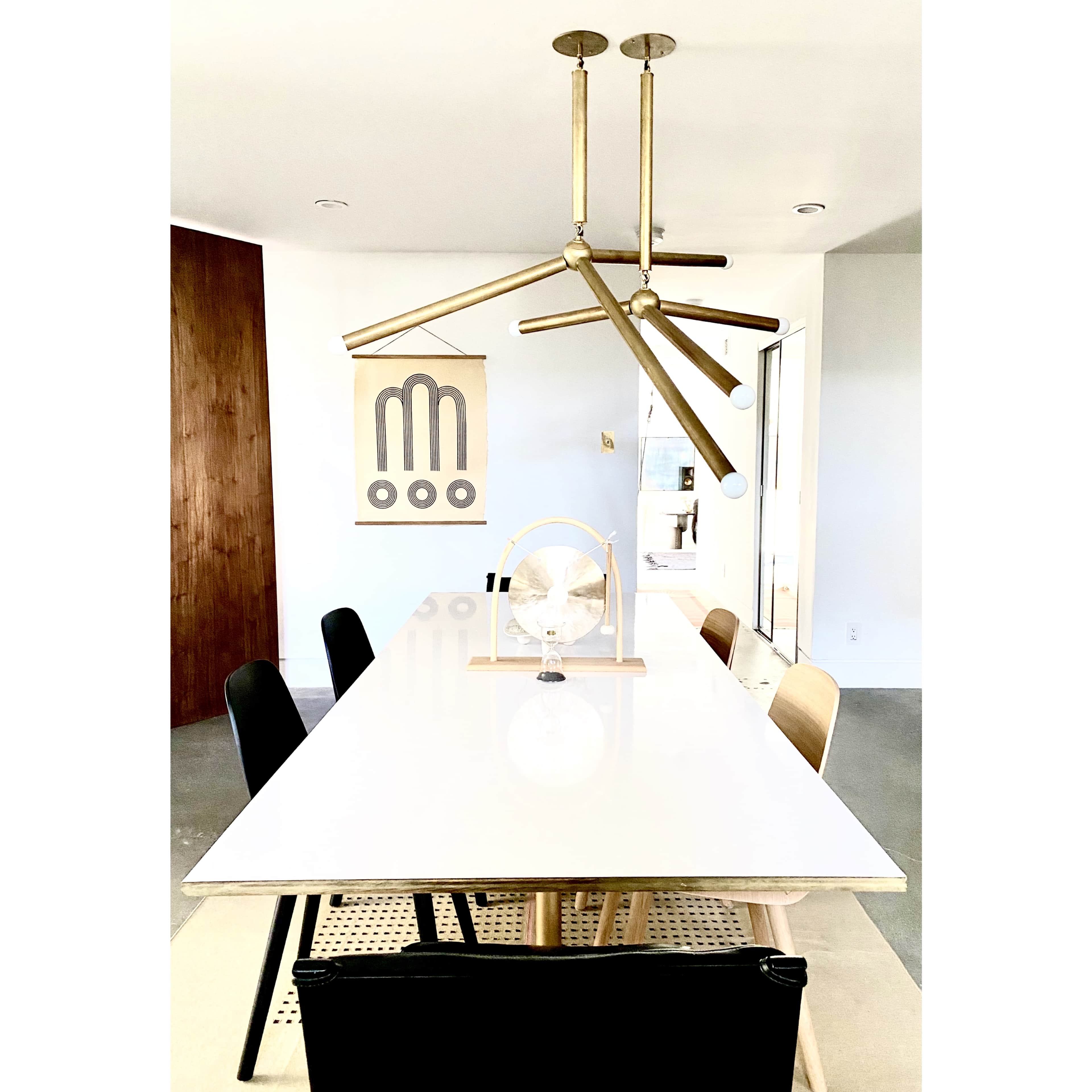 A modern dining room with a long white table, black and wooden chairs, and a unique ceiling light fixture above it.