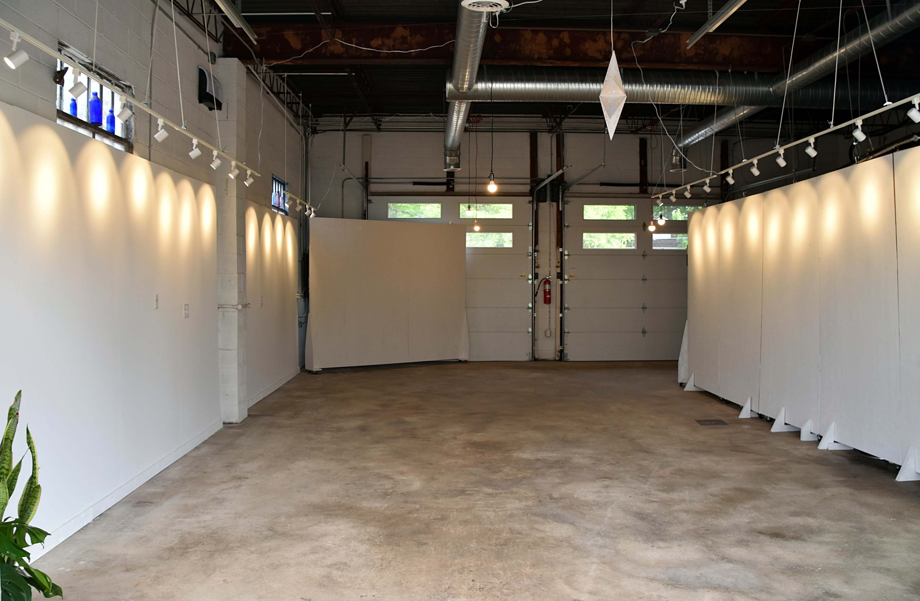 The image shows a large, open art gallery with white walls, concrete floors, and track lighting illuminating the space.