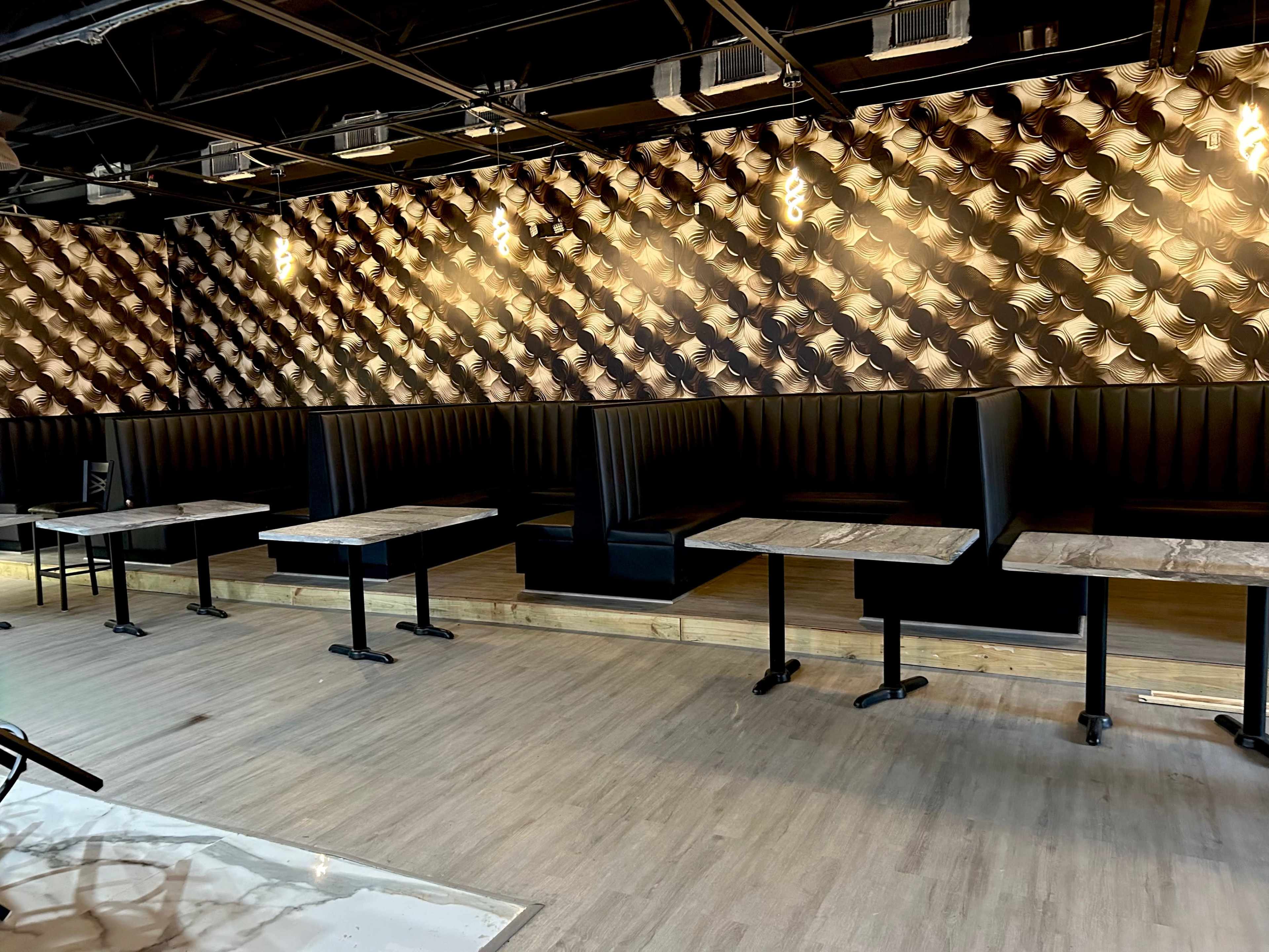 A modern restaurant interior featuring black booths and tables arranged against a patterned wall.