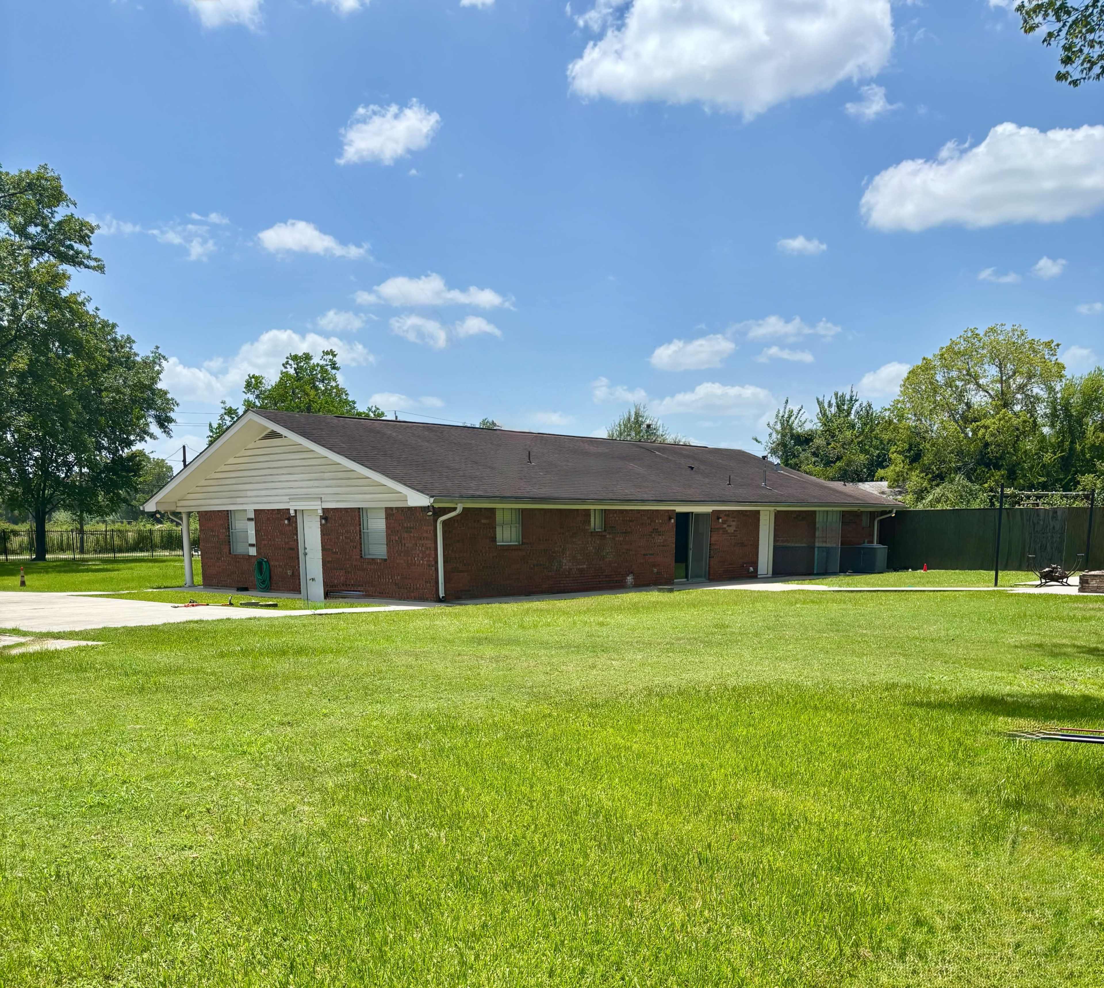A single-story brick building with a sloped roof is situated on a grassy lawn under a partly cloudy sky.
