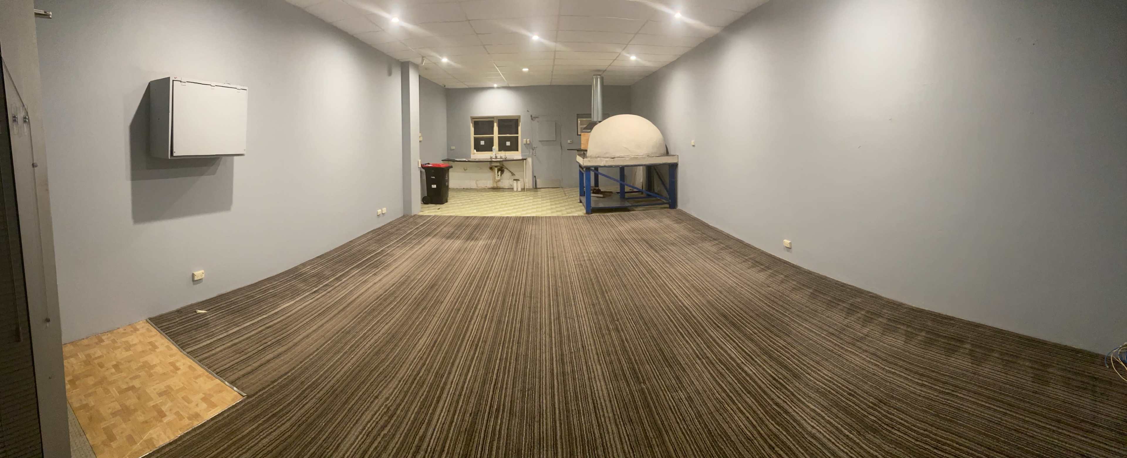 A wide, empty room with gray walls, a patterned carpet, and a round structure on a blue table at the far end.