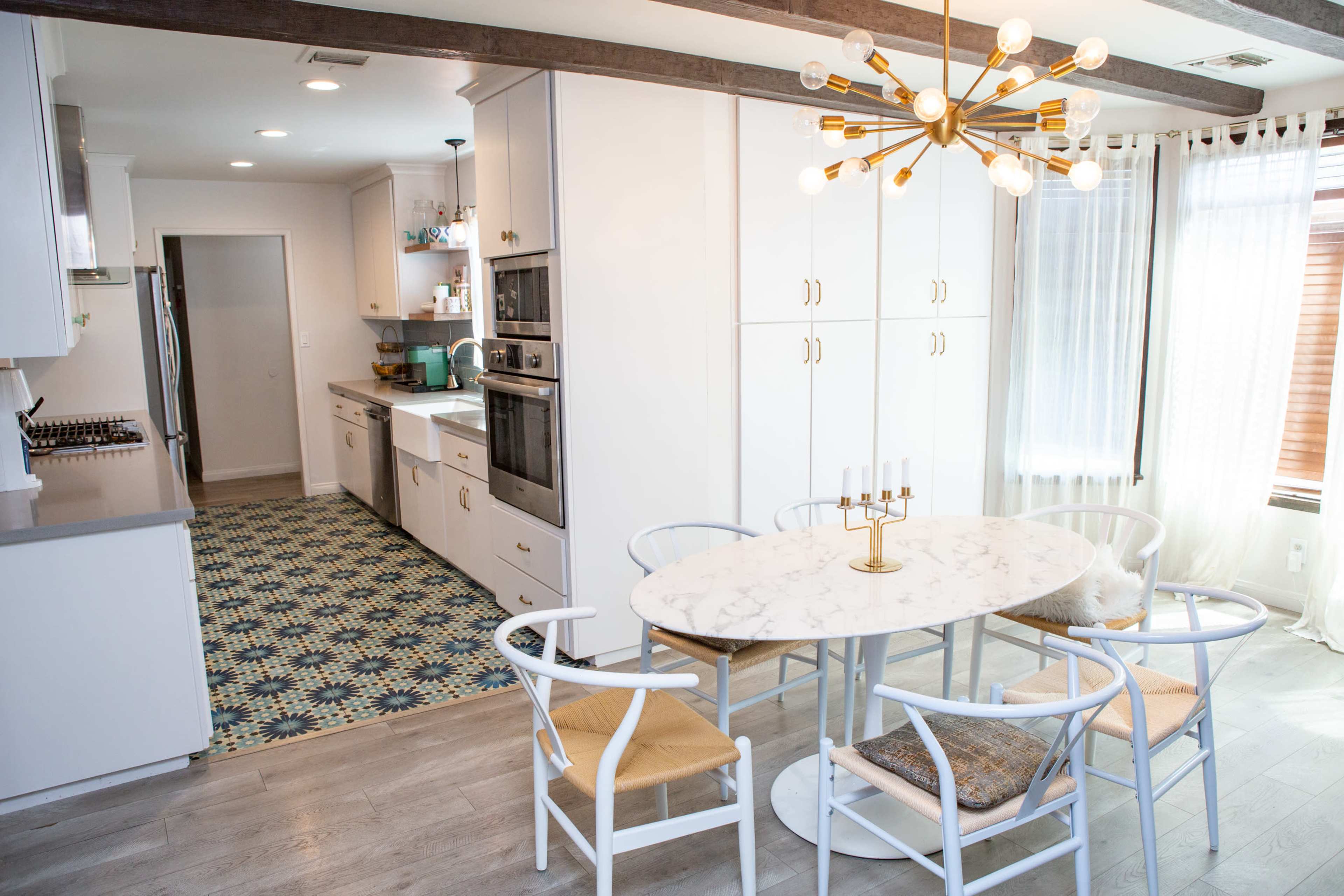 A modern kitchen and dining area featuring an oval marble table surrounded by white chairs, with cabinetry and appliances in a light color scheme.