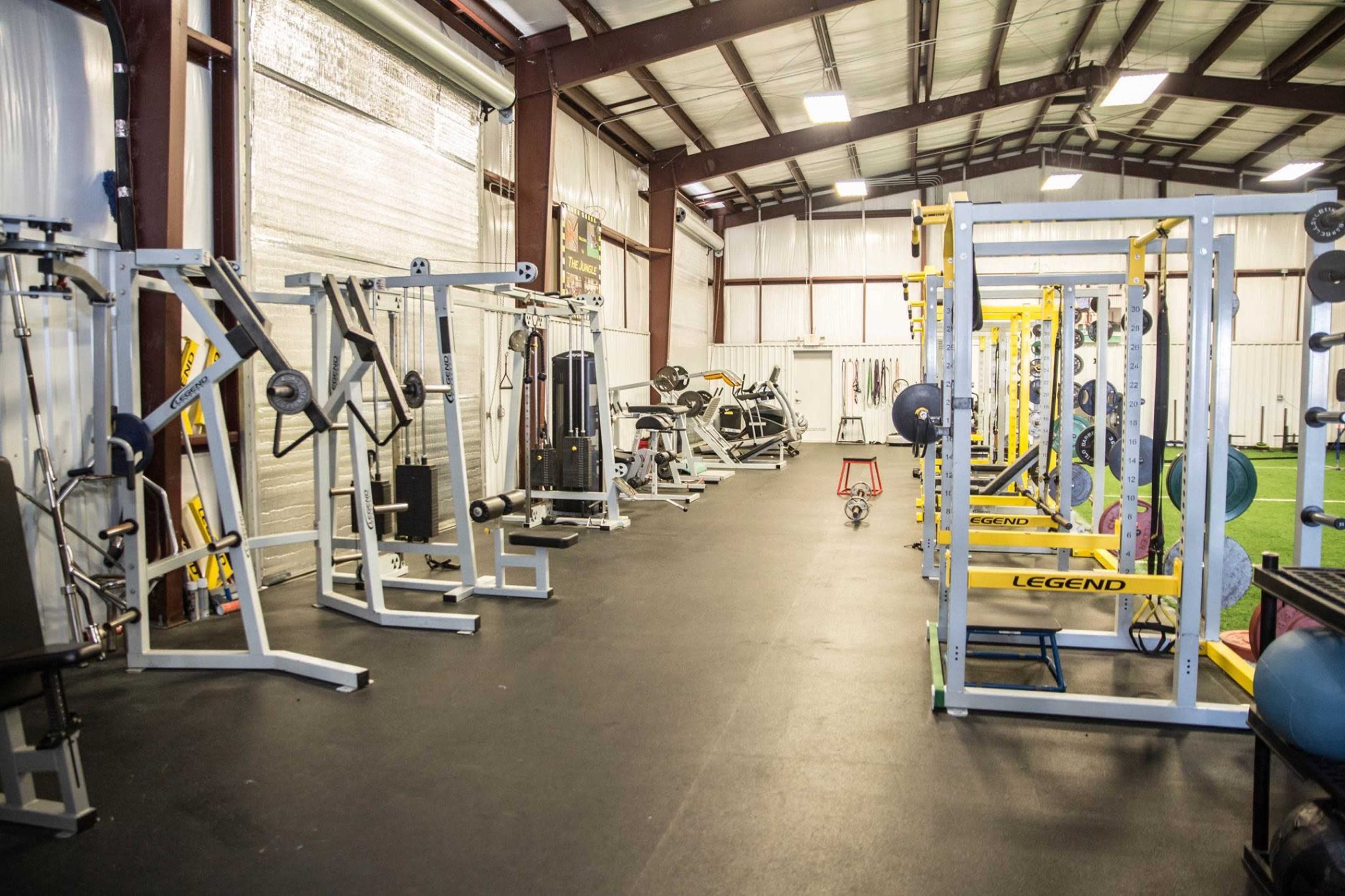 An indoor gym filled with various weightlifting equipment and workout machines arranged along the walls of a large, open space.