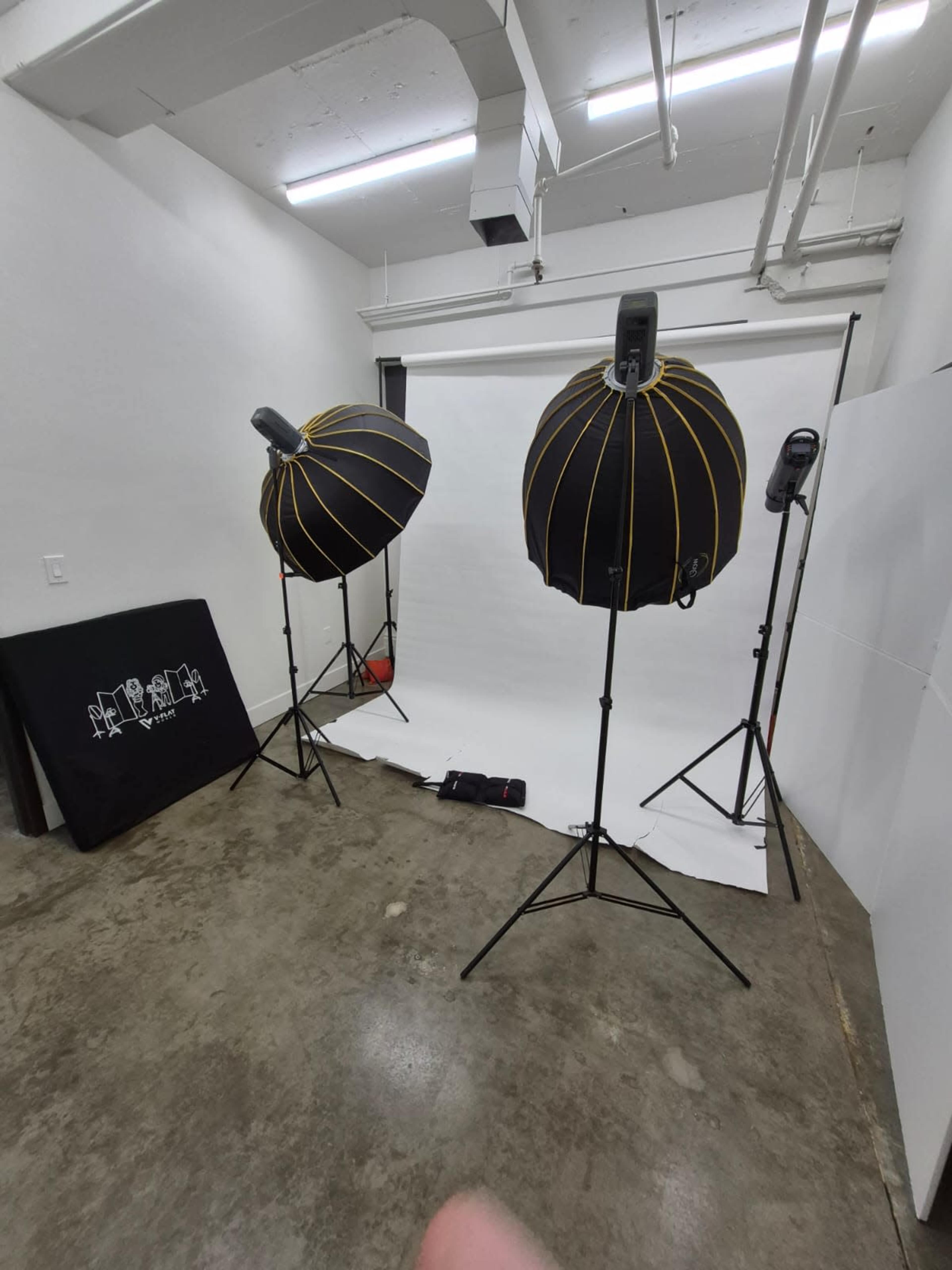 The image shows a photography studio setup with two softbox lights and a white backdrop.