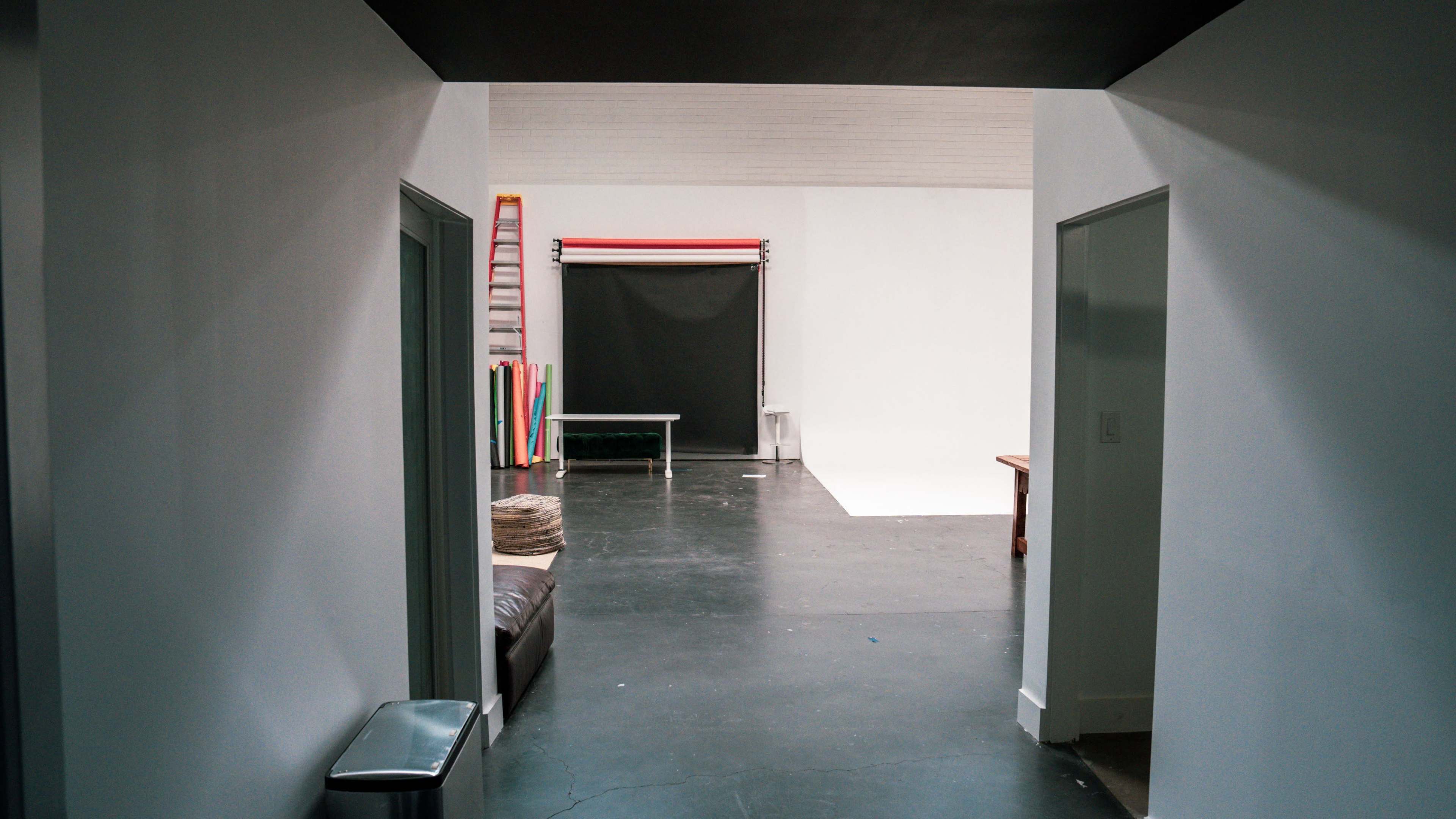 The image shows a spacious photography studio with a black floor, studio backdrop, and various colored props arranged in the background.