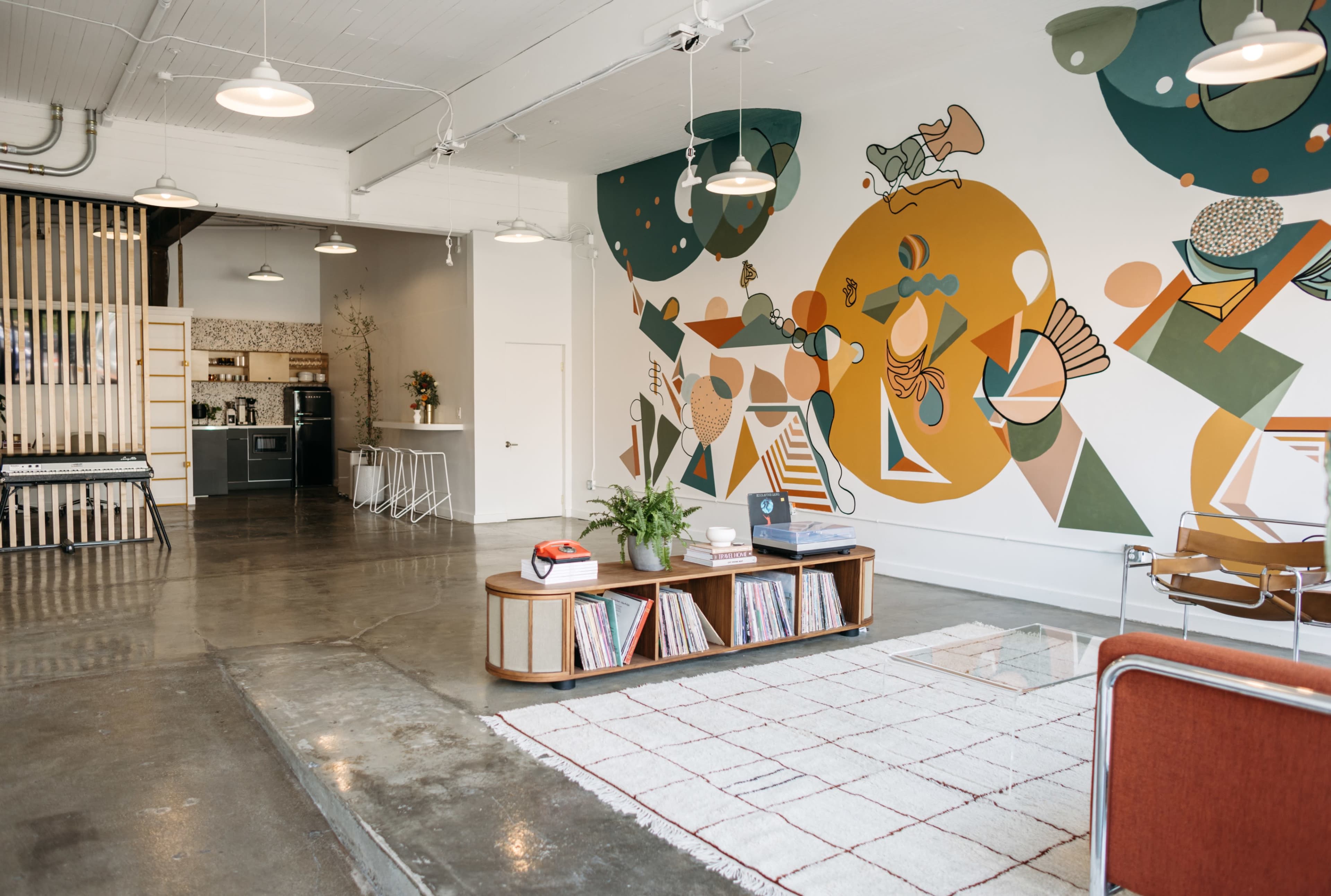 A spacious room features a modern design with a colorful mural on one wall, a coffee table with vinyl records, and stylish furniture.