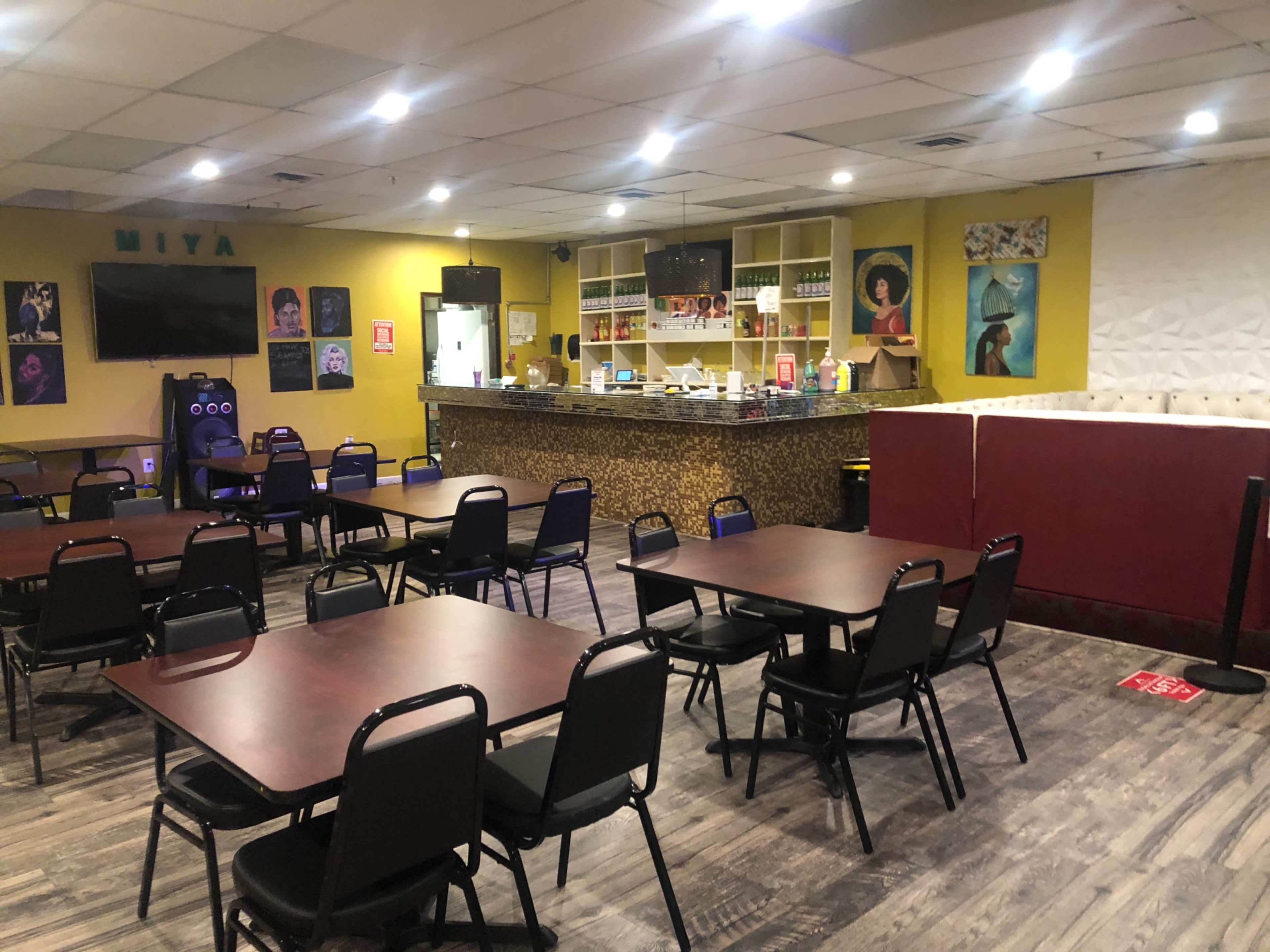 A spacious dining area with multiple tables and chairs, featuring a counter area with shelves and a television on the wall.