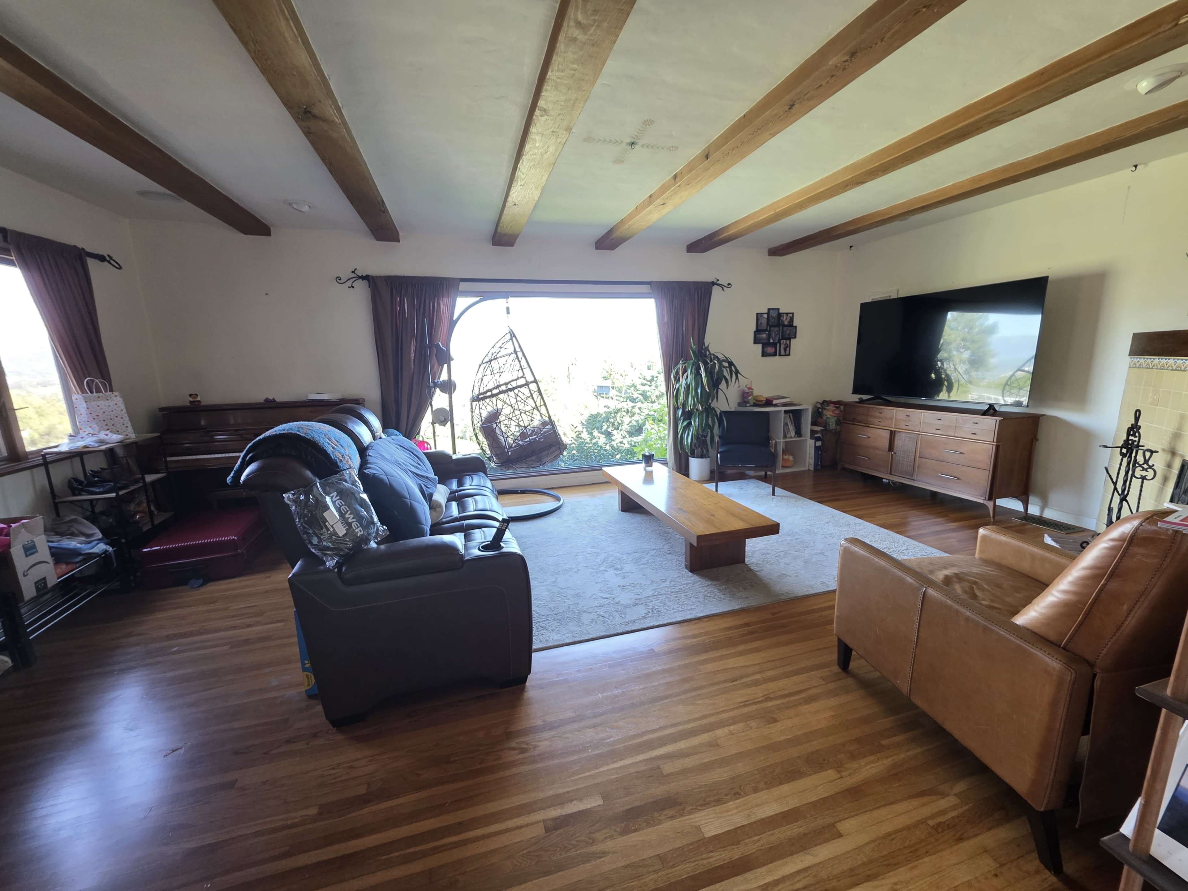 The image depicts a spacious living room featuring a large window with a view, two couches, a wooden coffee table, and a television mounted on the wall.