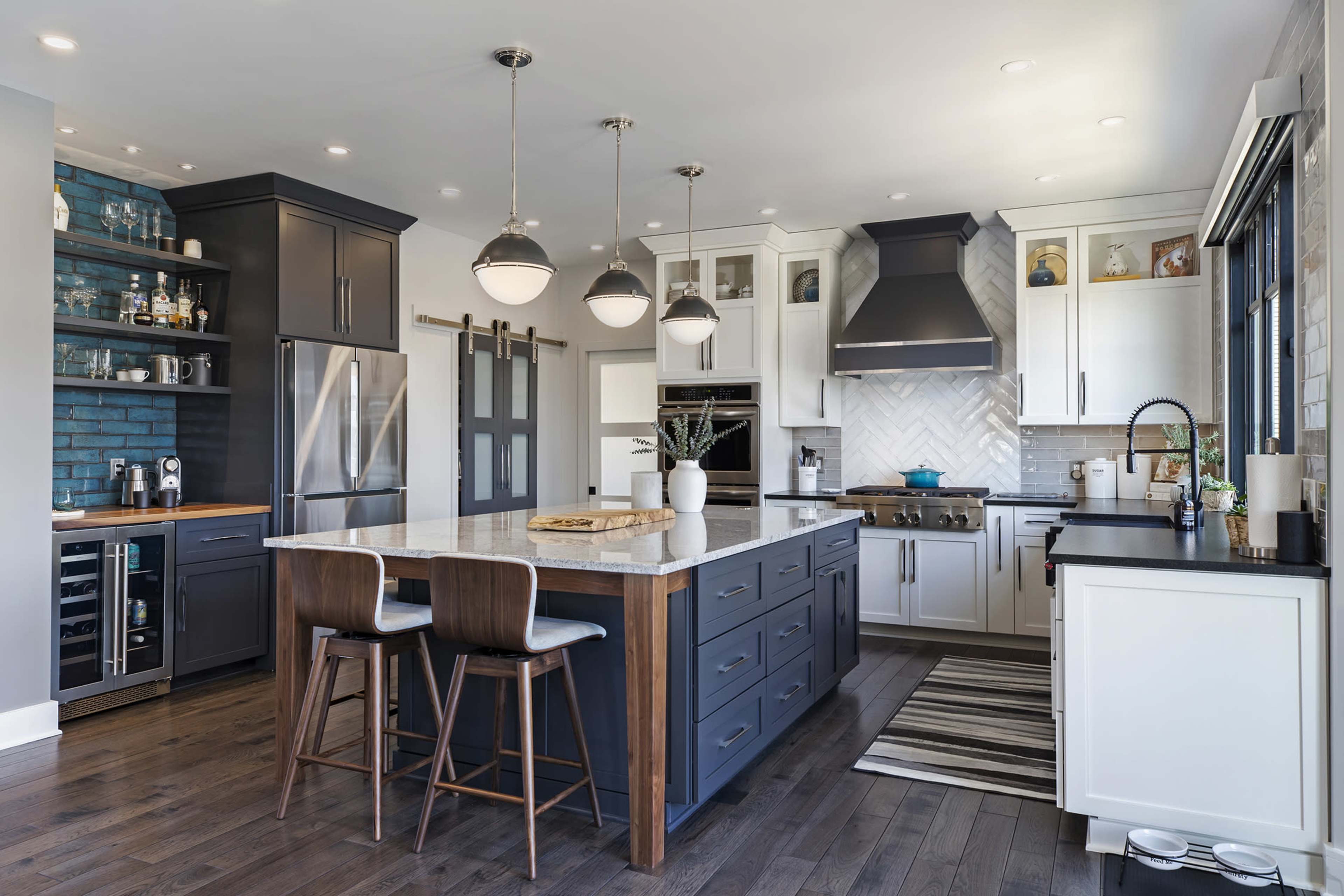 A modern kitchen featuring a central island with seating, dark cabinetry, stainless steel appliances, and a mix of blue and white accents.