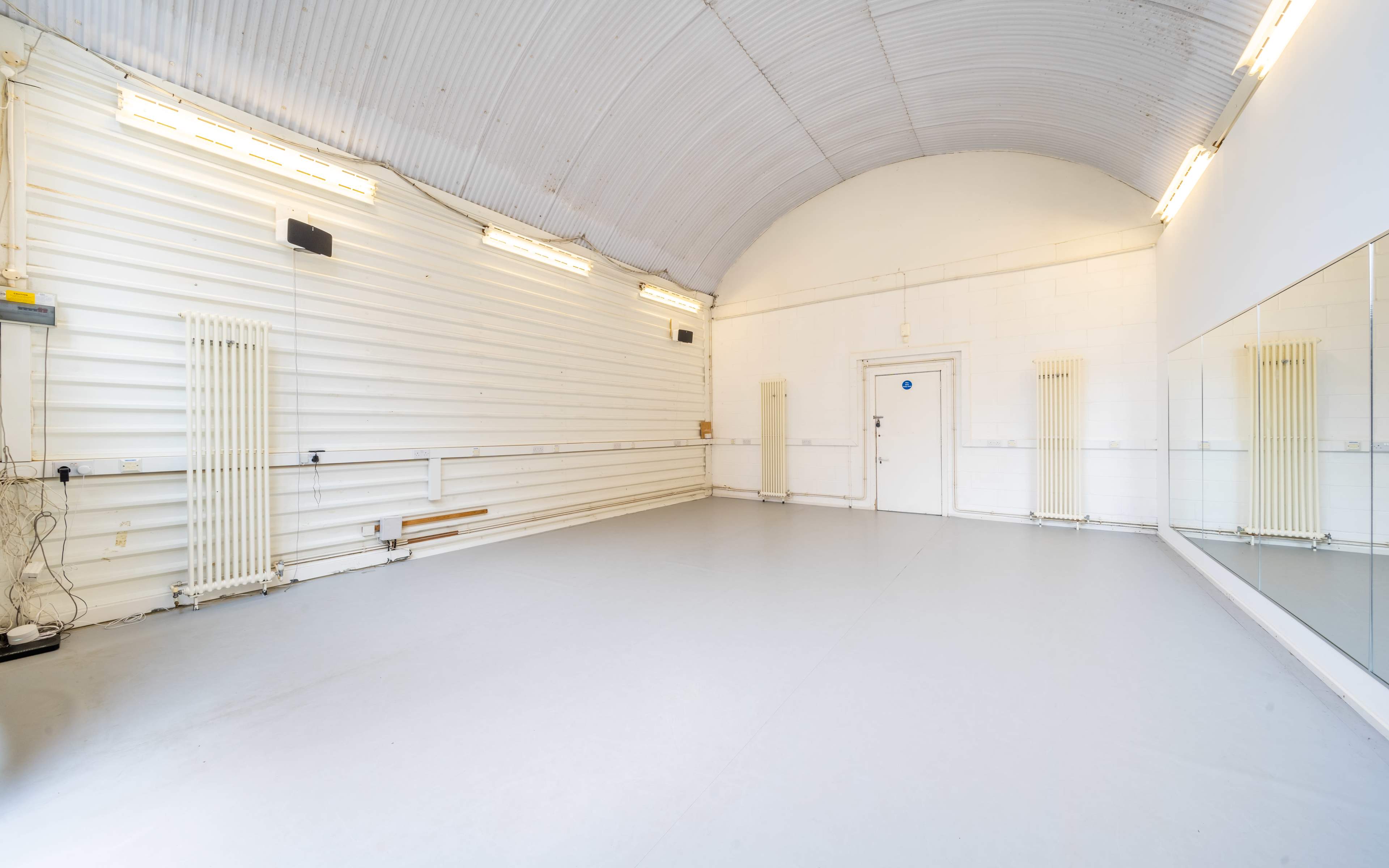 An empty studio space with white walls, a mirrored section, and overhead lighting.