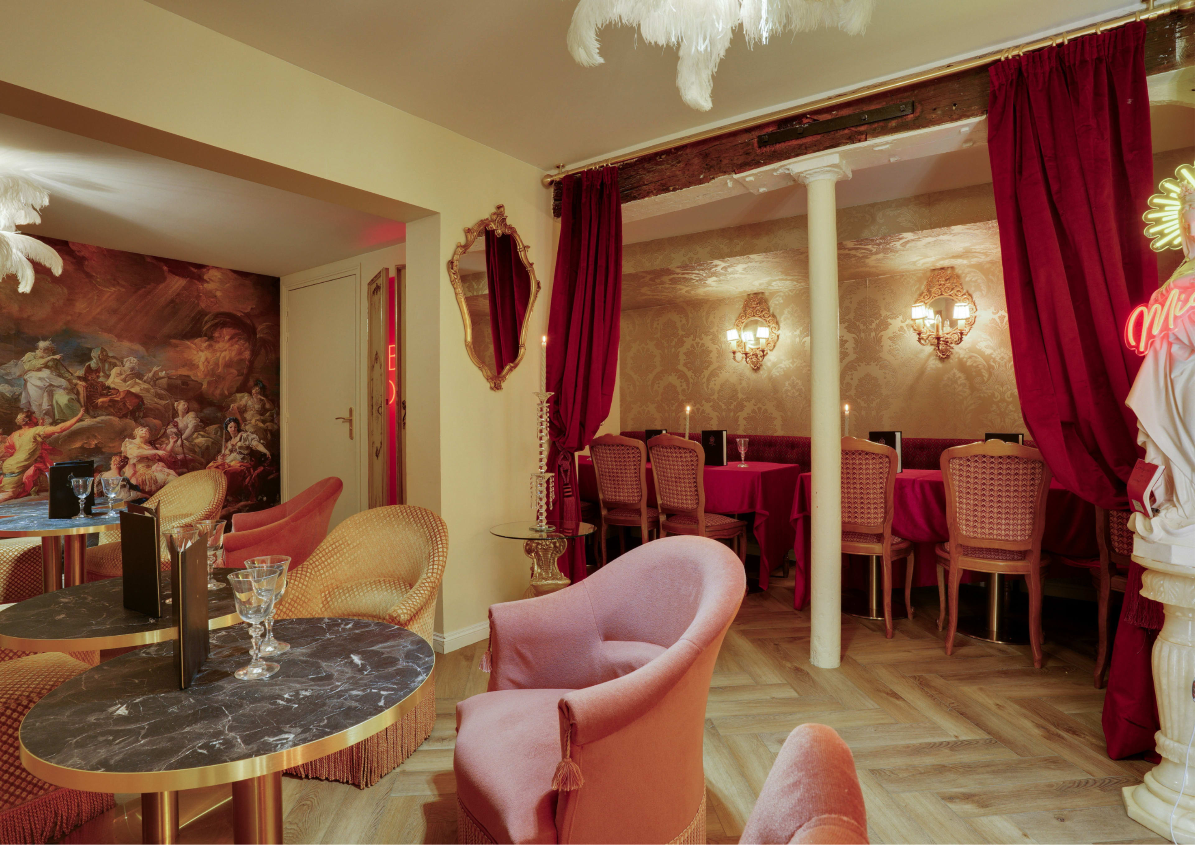 The scene features an elegantly decorated cafe with plush pink chairs, marble tables, and red curtains, creating an intimate atmosphere with decorative wall art and soft lighting.