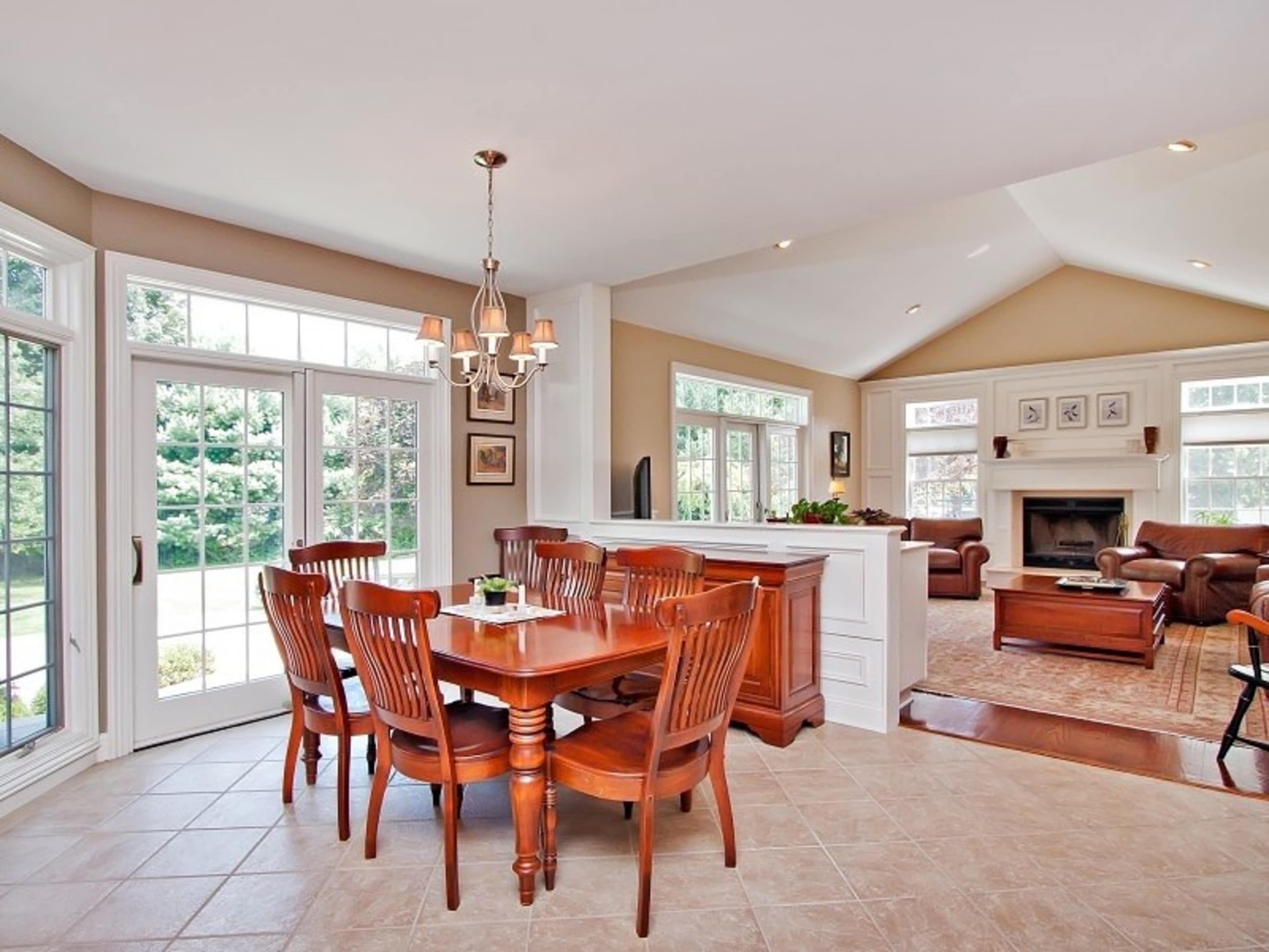 A spacious dining area with a wooden table surrounded by chairs, adjacent to a living room featuring a fireplace and large windows.