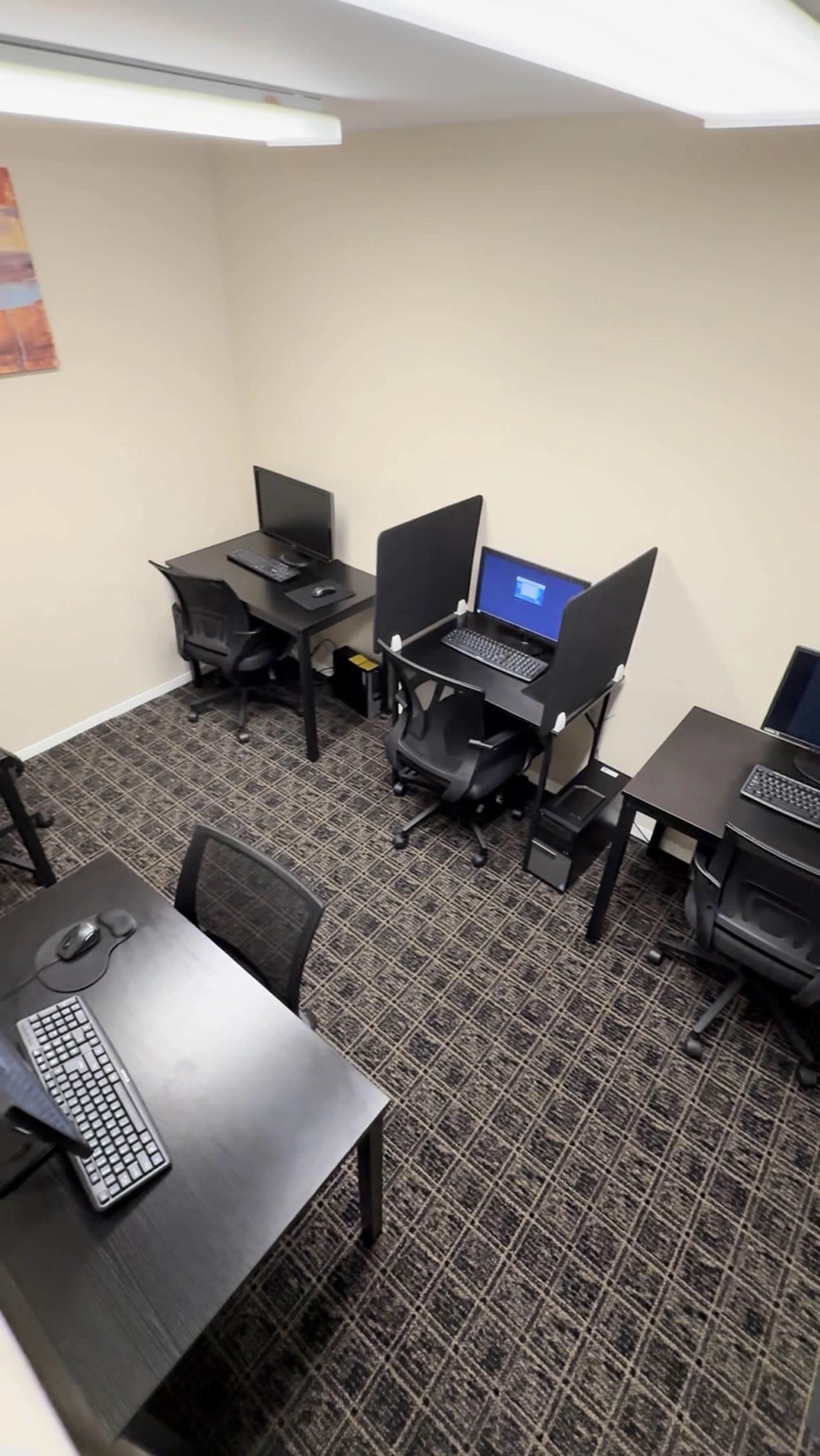 The image shows a small office space with several desks equipped with computer monitors and chairs.