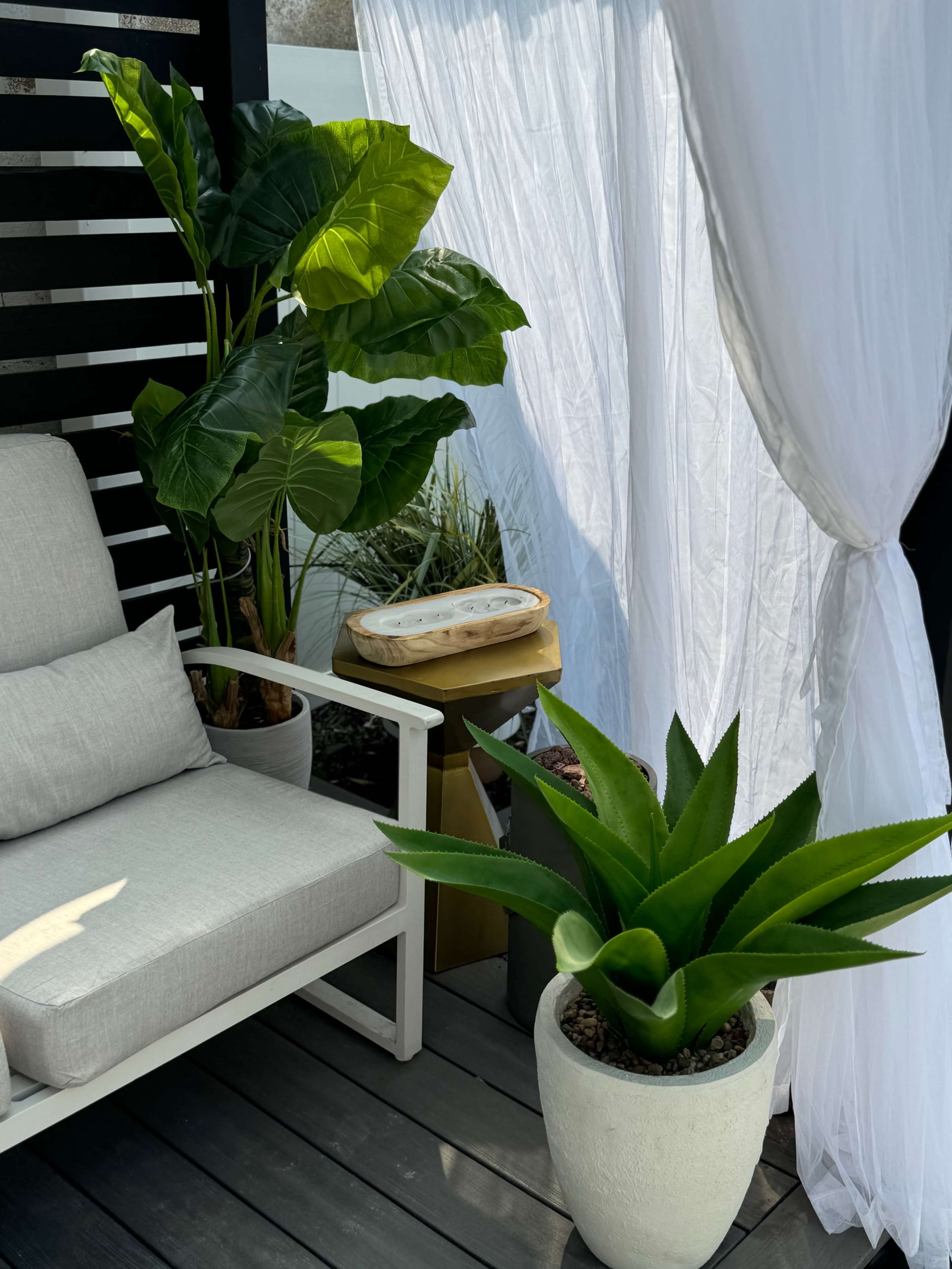 A cozy outdoor seating area features a white armchair, green plants, and flowing white curtains.