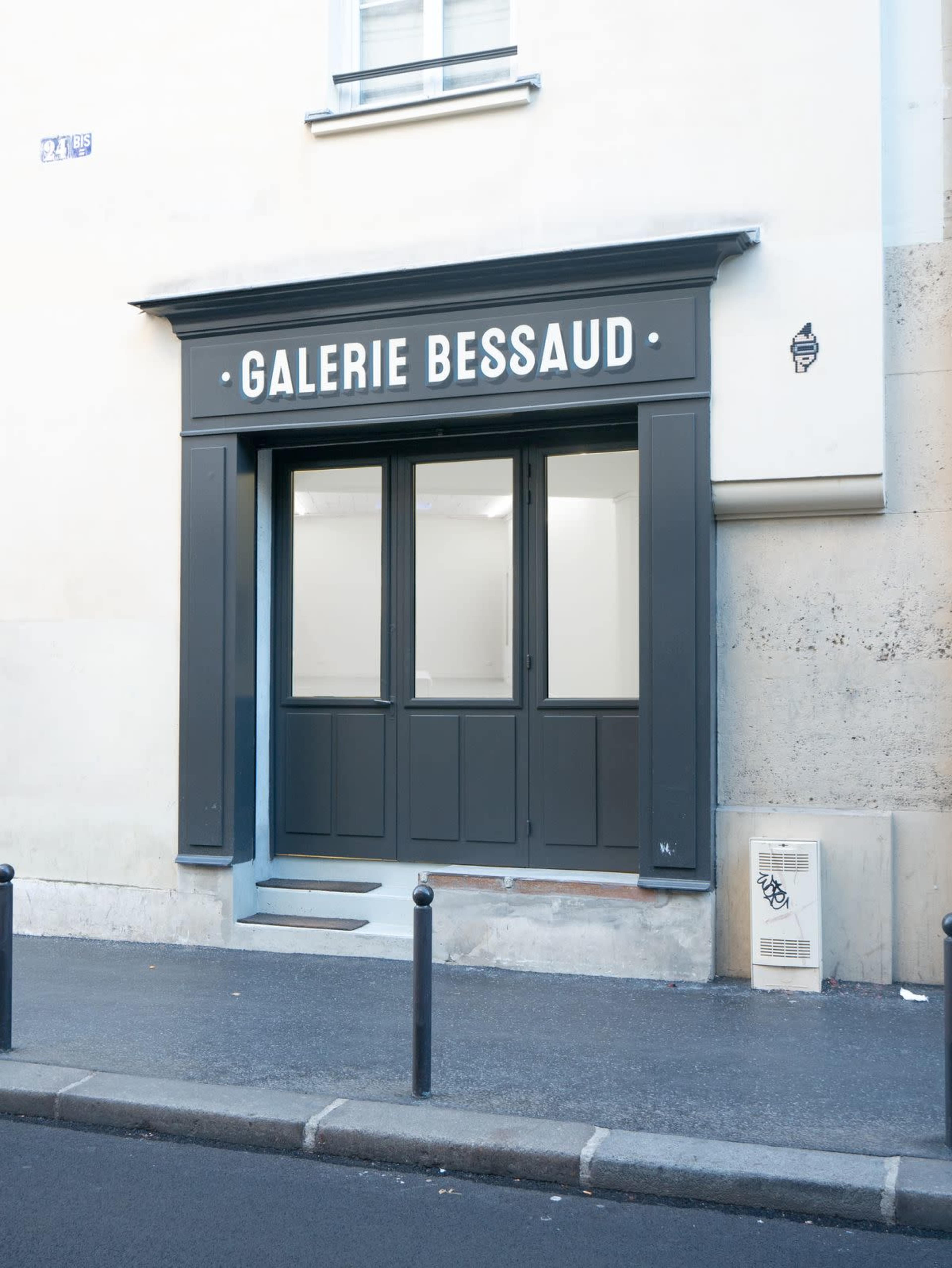 The image shows the entrance of a gallery named "Galerie Bessaud," featuring a dark facade and large glass doors, set against a plain building wall.
