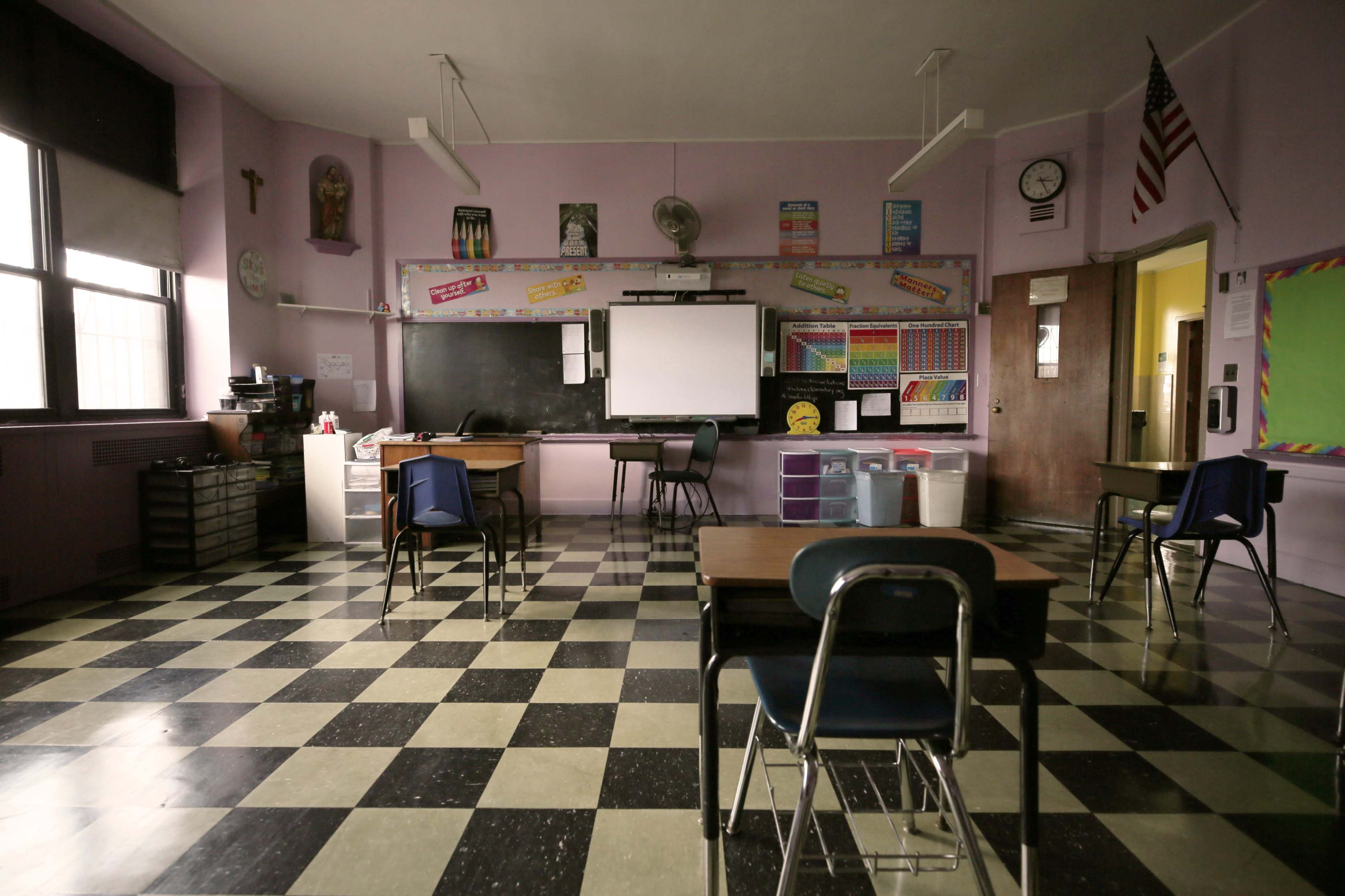 A classroom with purple walls, a blackboard, empty desks, and a large clock on the wall.