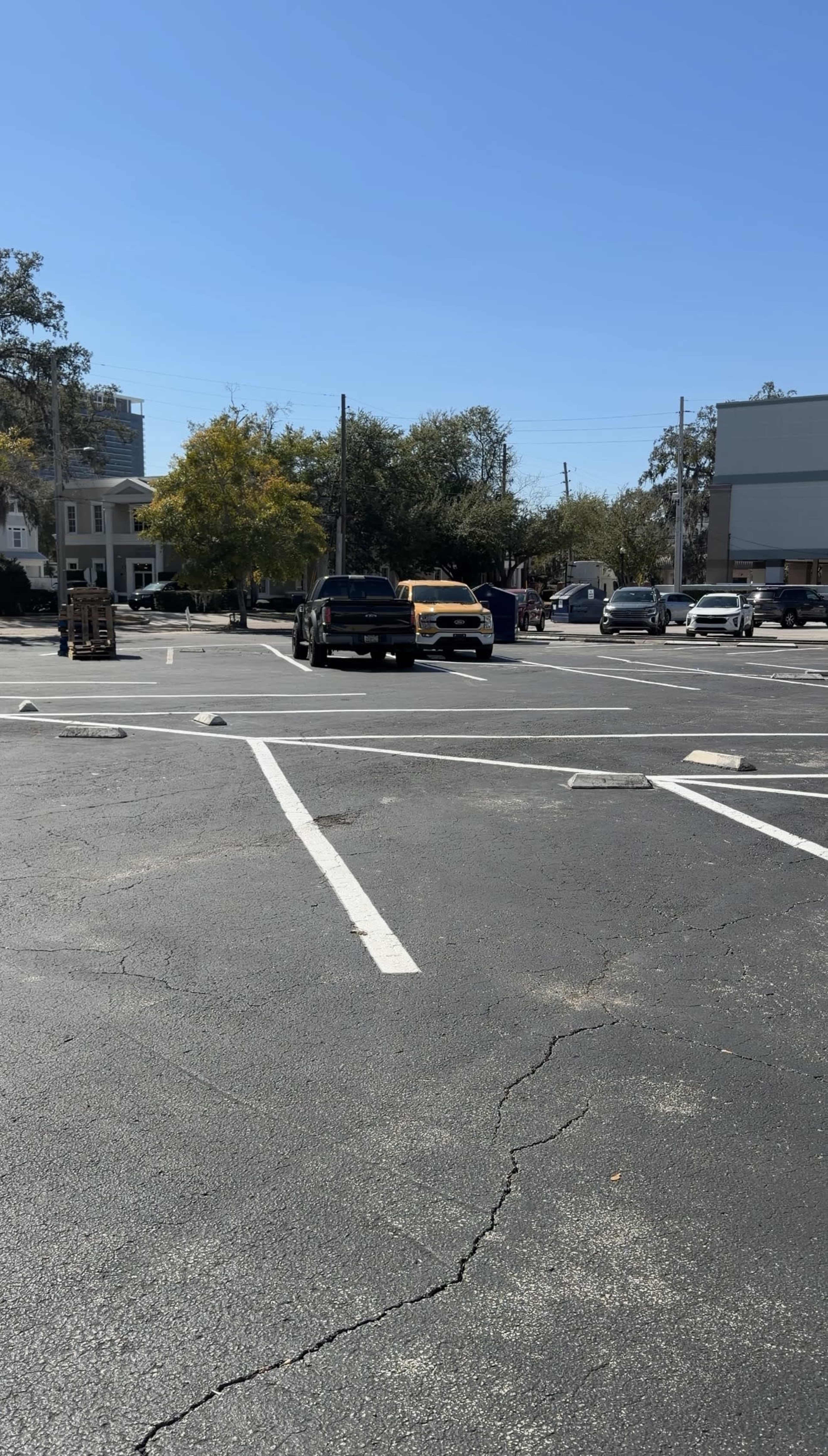 A parking lot with several vehicles, including a black truck and a yellow vehicle, under a clear blue sky.