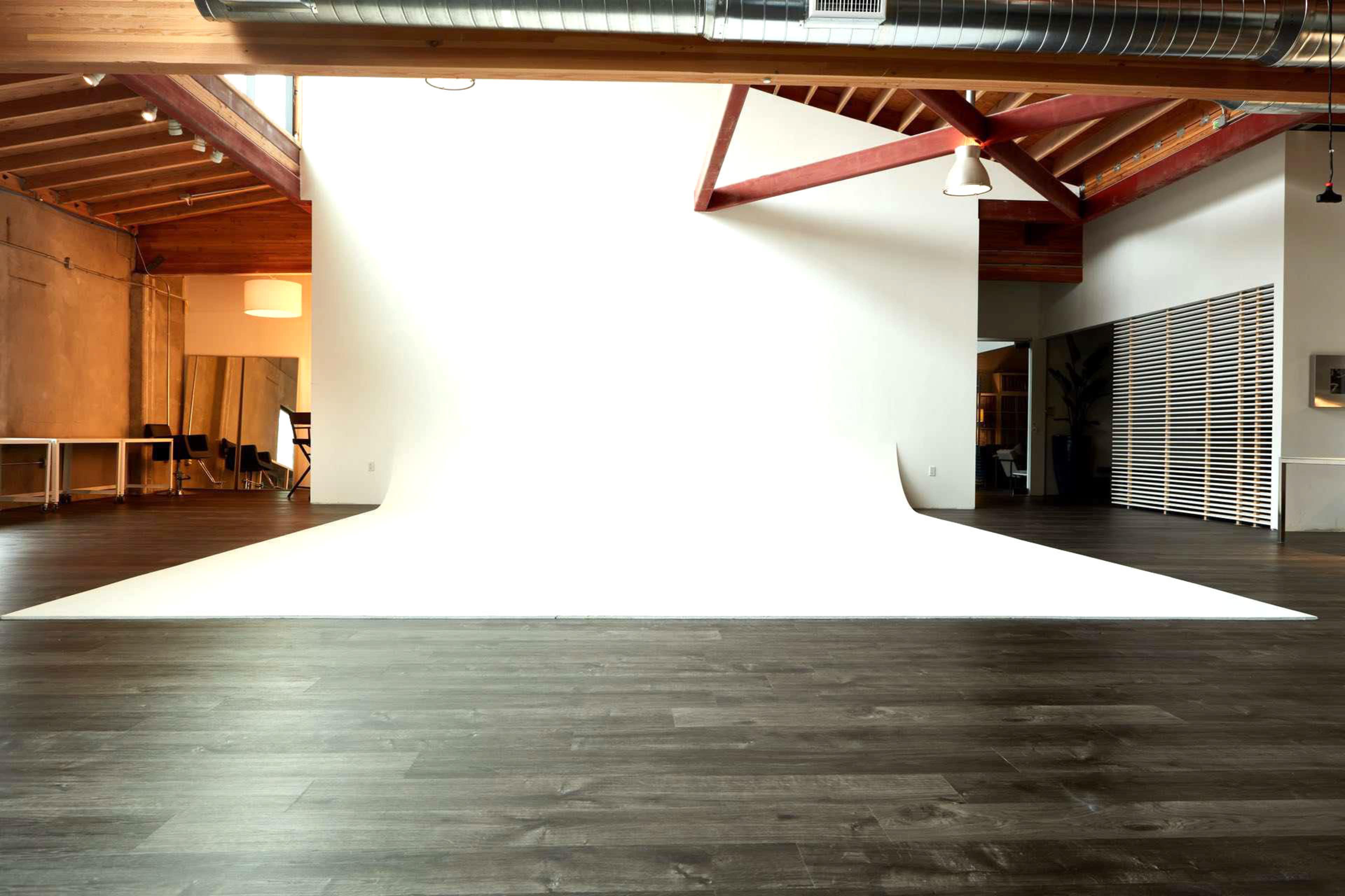 A spacious studio with a large white backdrop and wooden floors.