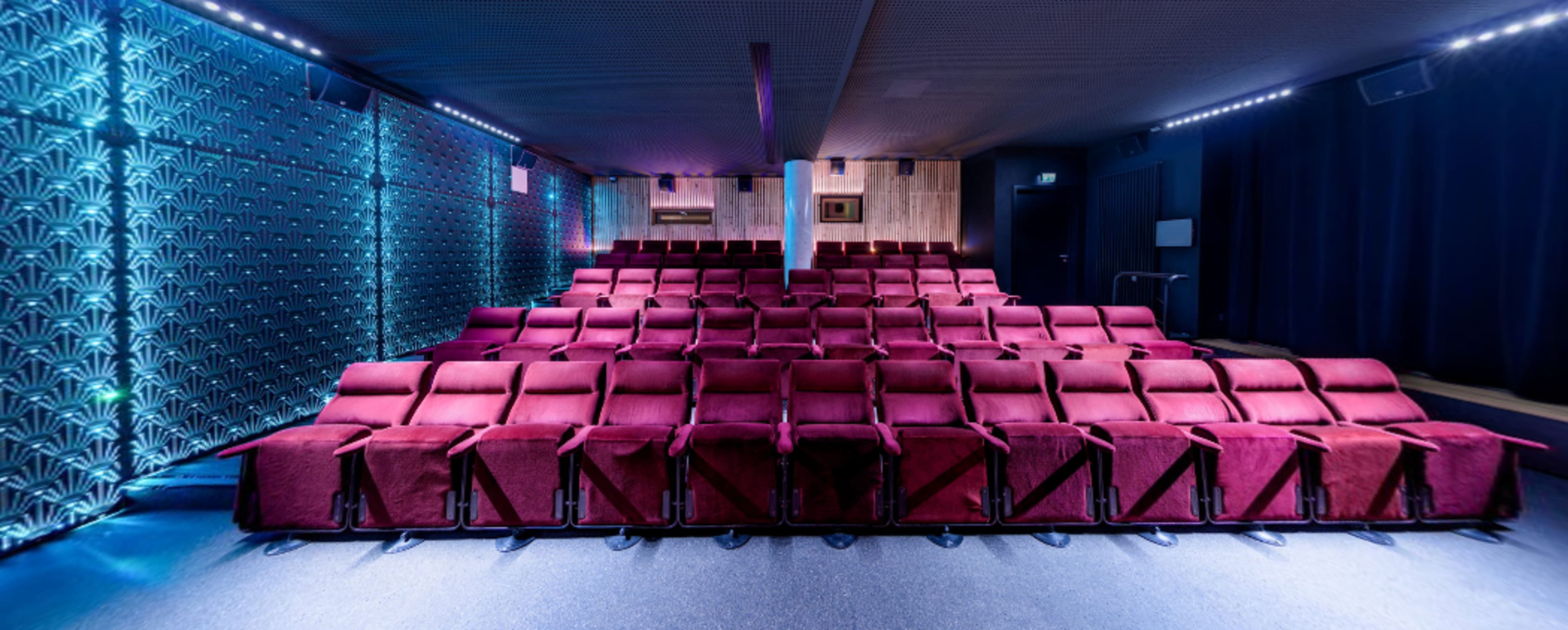 A row of red upholstered theater seats arranged in a dimly lit auditorium.