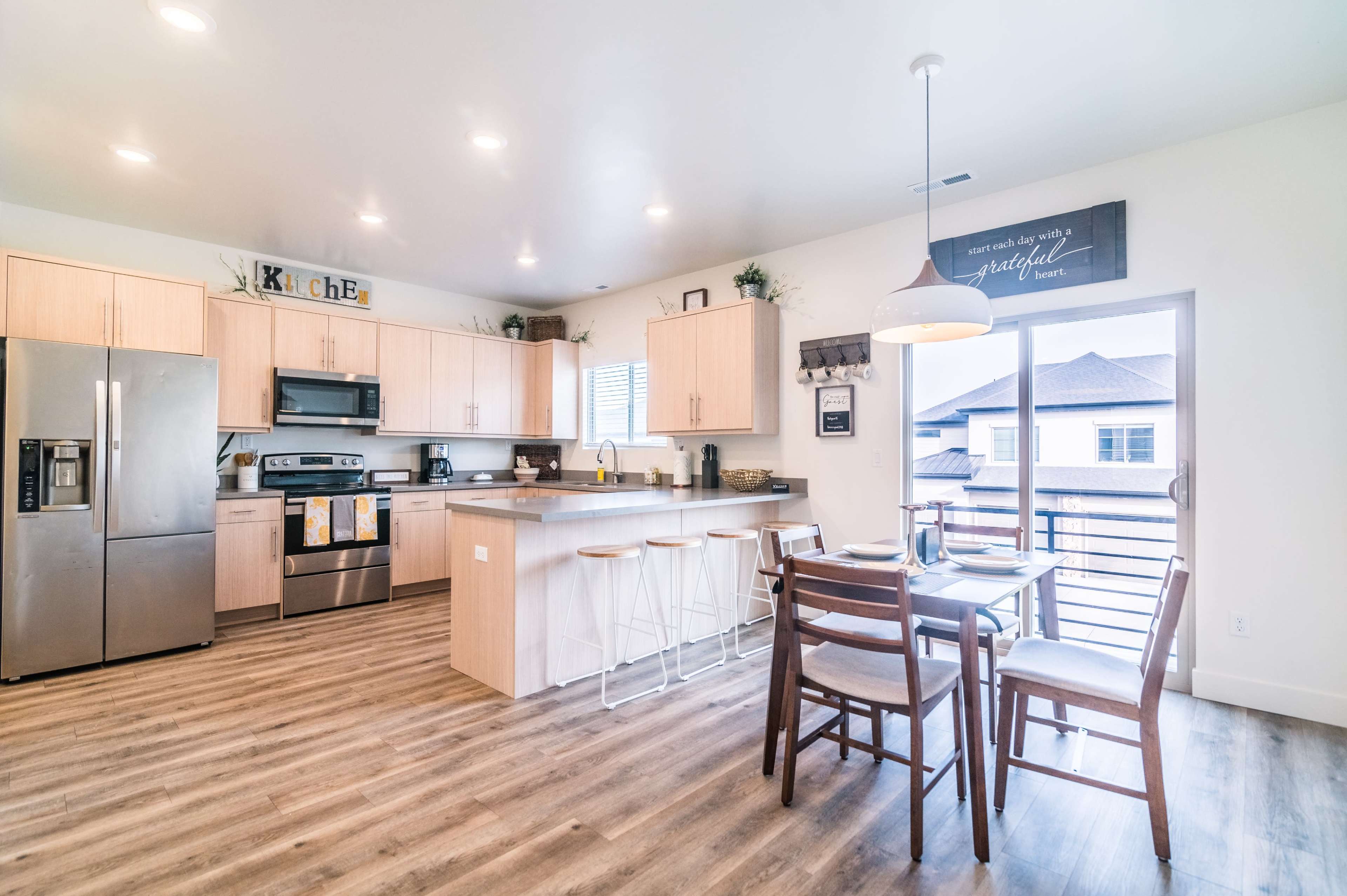 A modern kitchen features wooden cabinetry, stainless steel appliances, and a dining area with a table and chairs.