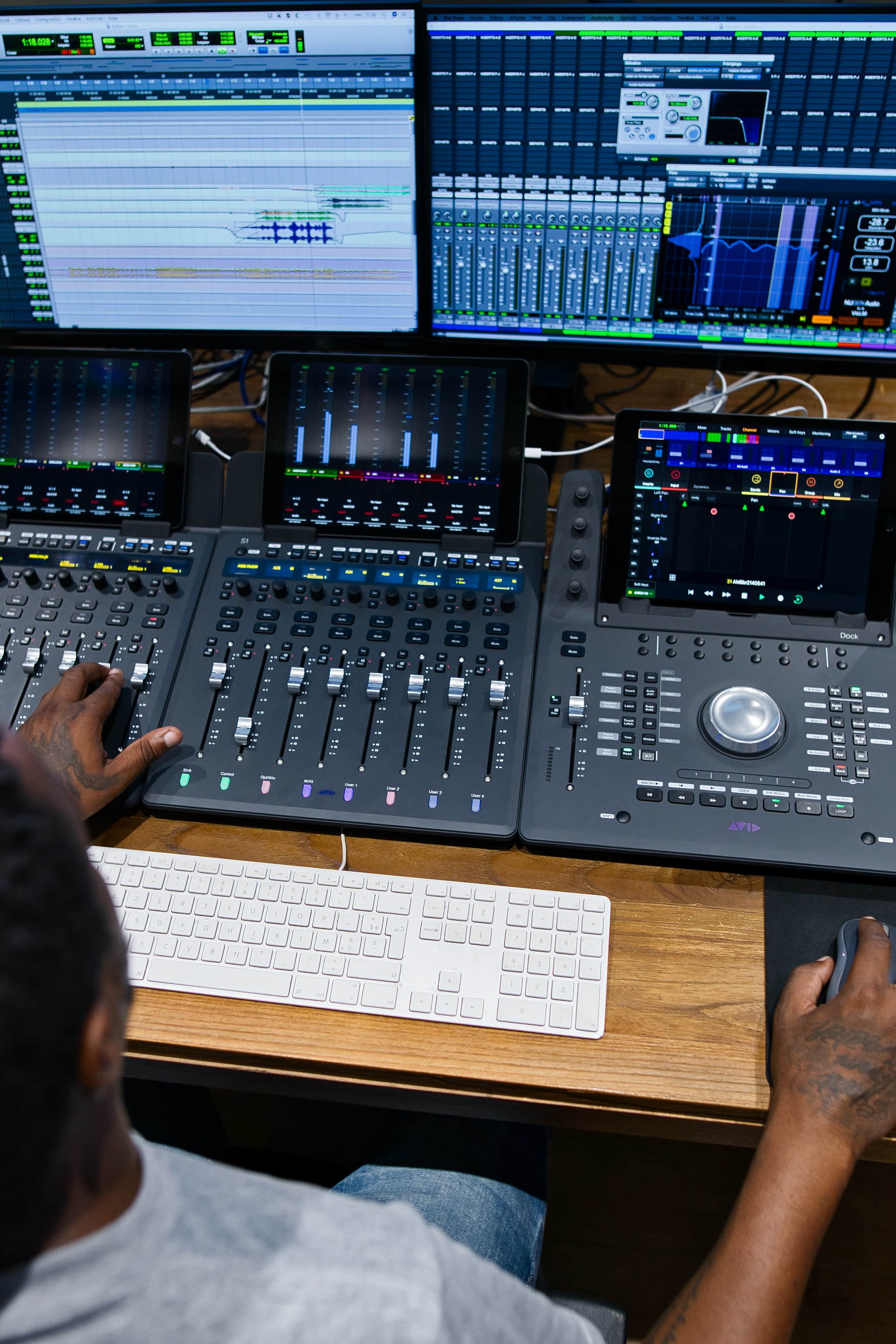 A person is using a digital audio workstation setup with multiple screens and a mixing console.