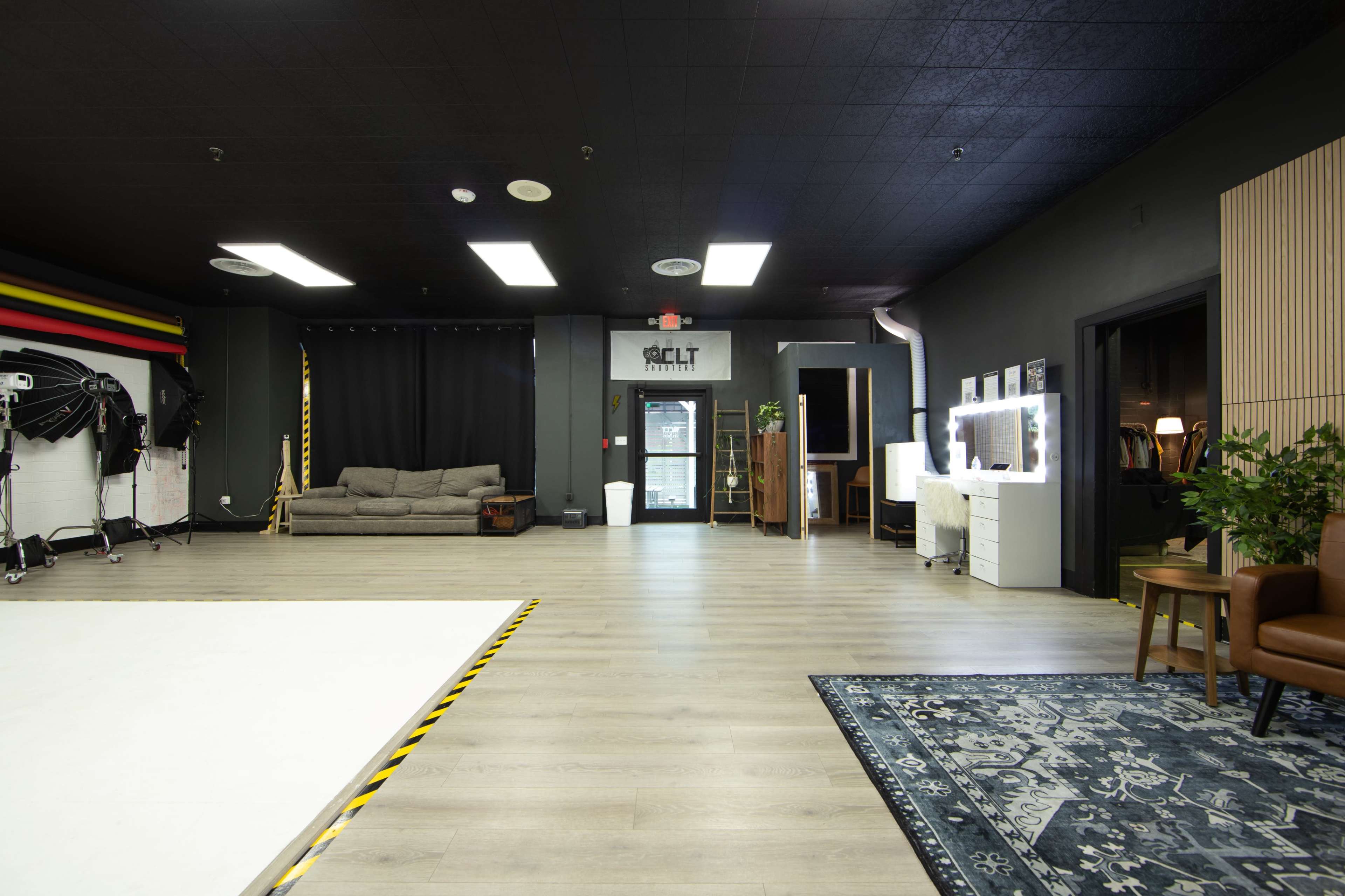 The image shows a spacious, dimly lit studio with a large white area for activities, a couch, and various lighting and mirror setups along the walls.