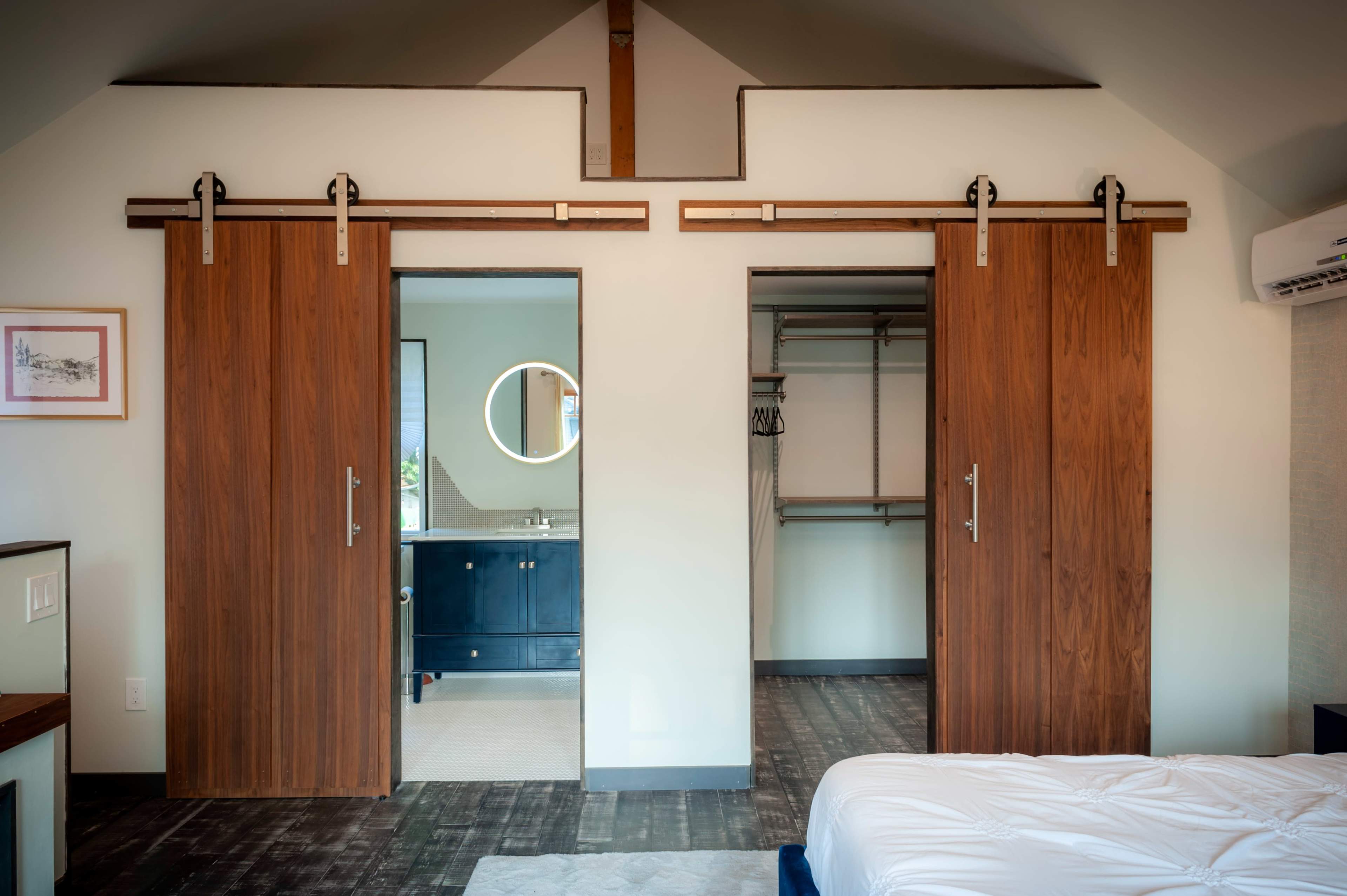 A bedroom with two sliding wooden doors leading to a bathroom and a closet, with a bed positioned in the foreground.
