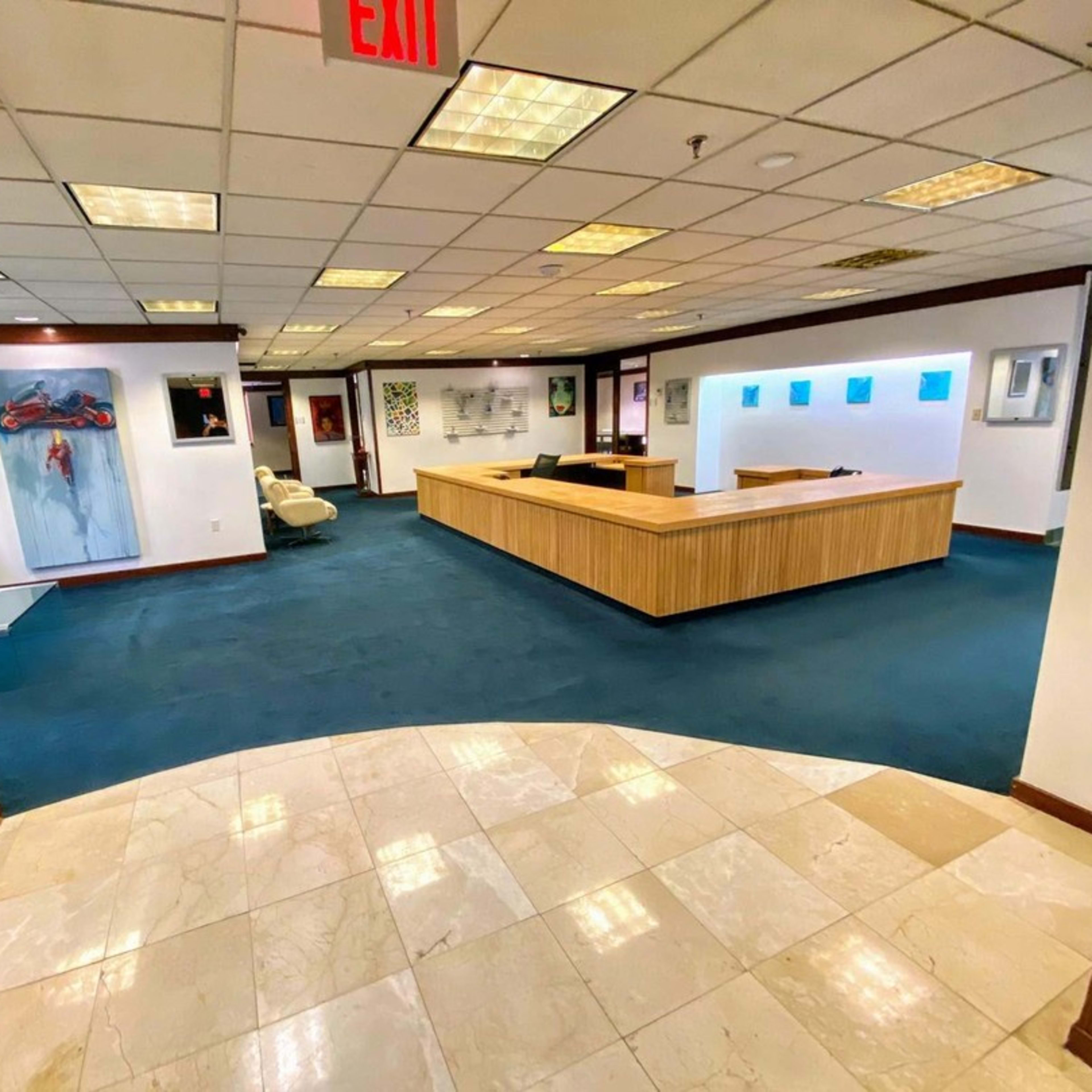 The image shows a spacious office interior with a reception area featuring a wooden desk, artistic wall decorations, and carpeted flooring.