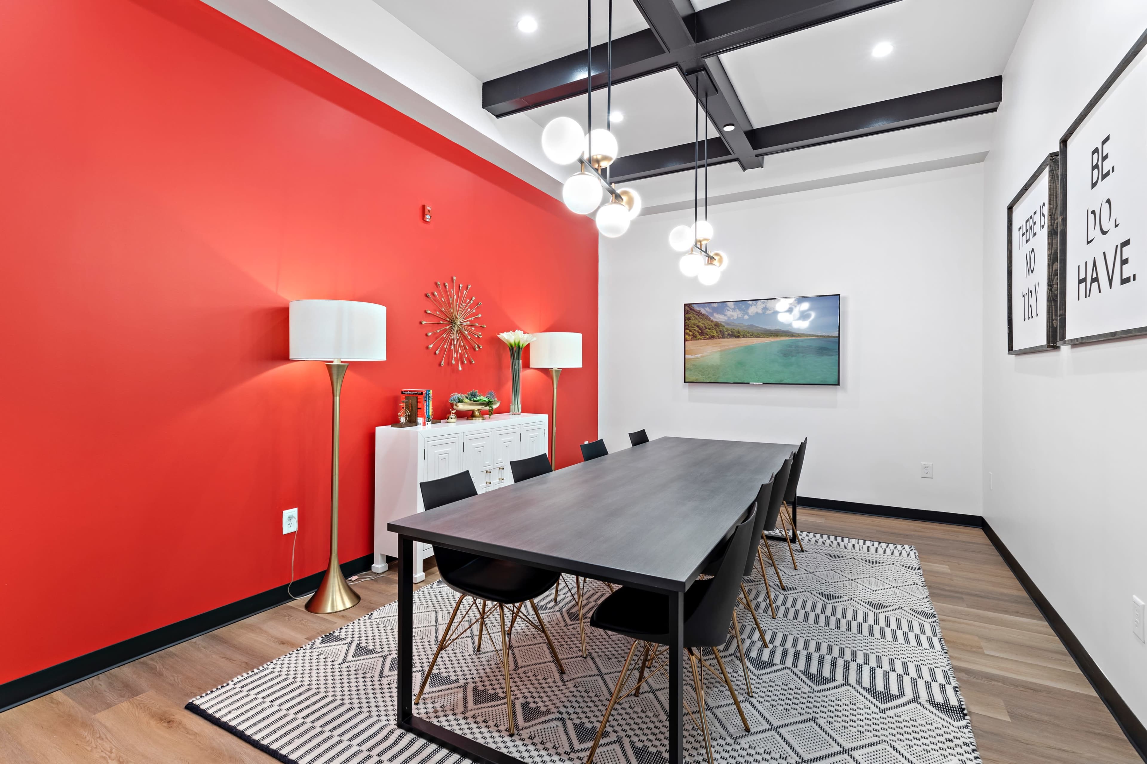 A modern conference room with a long table surrounded by black chairs, a red accent wall, and decorative lighting fixtures.