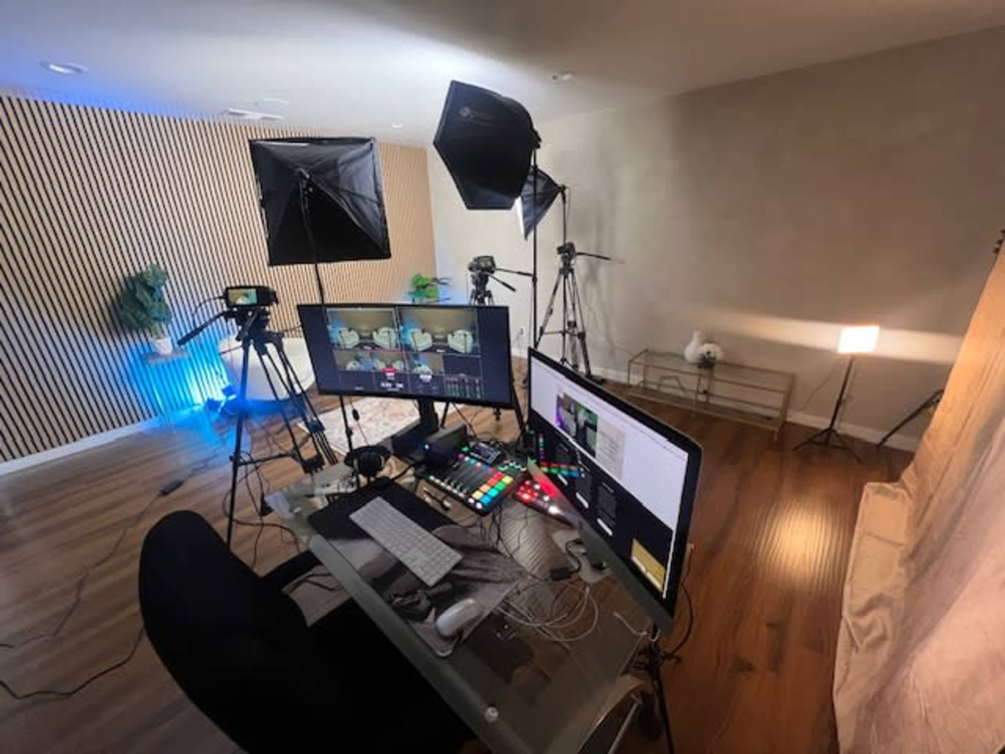 The image shows a modern video production setup with multiple cameras, lighting equipment, and a computer workstation in a well-lit room.