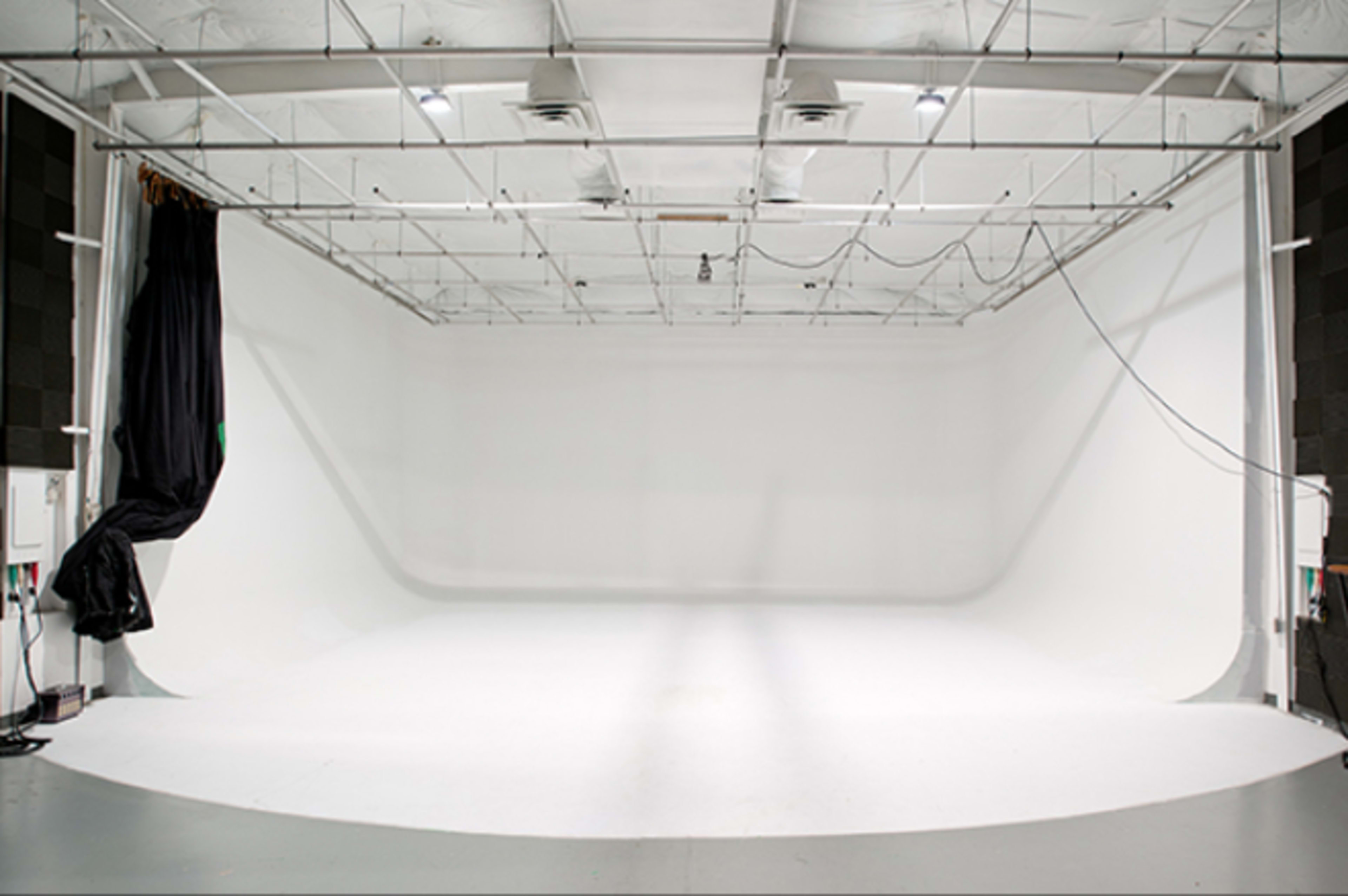 A spacious photo studio with a seamless white backdrop, high ceilings, and overhead lighting.