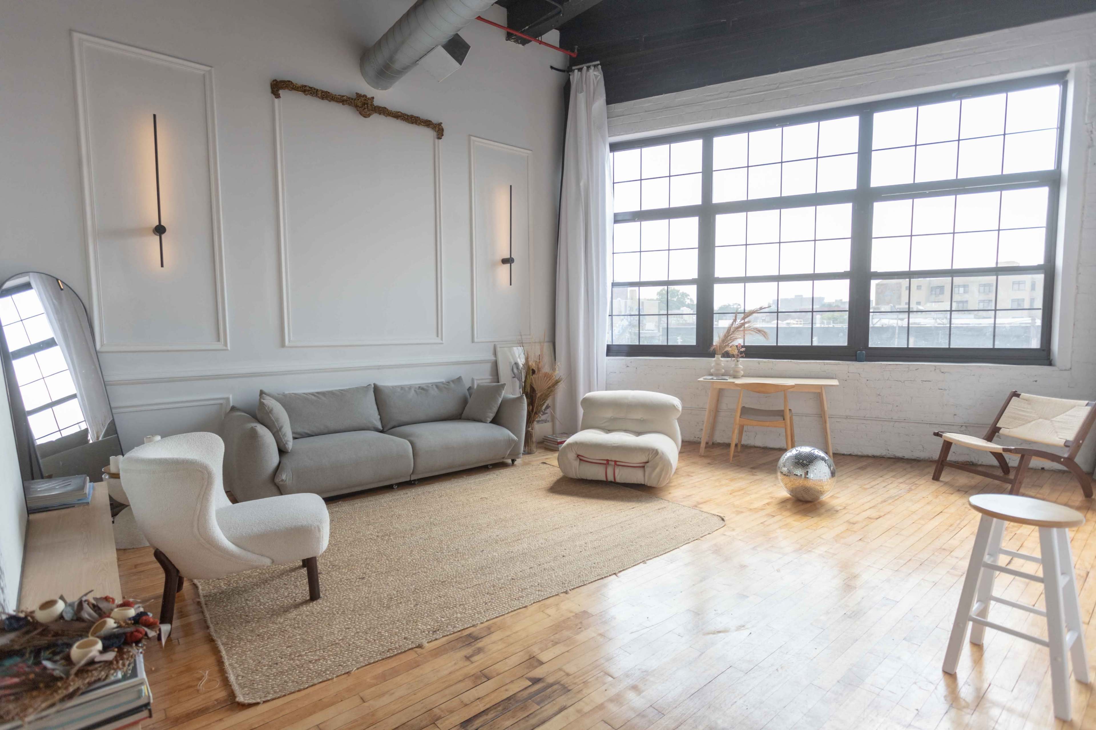 A spacious indoor area featuring a gray sofa, an upholstered chair, a round coffee table, and large windows that allow natural light to illuminate the wooden floor.